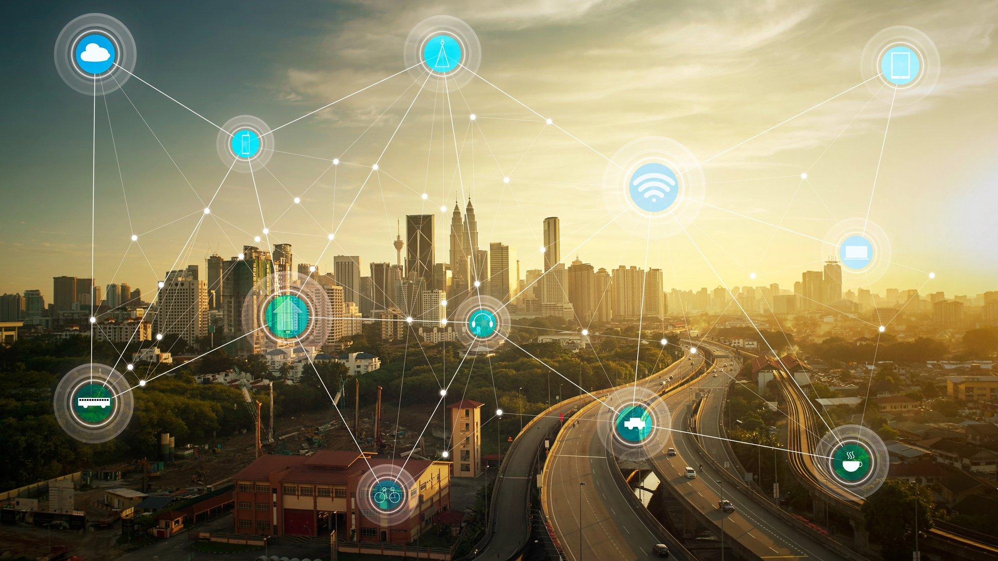 Die Skyline einer Stadt vor untergehender Sonne, darüber gelegt ein digitales Netz mit Symbolen für Wlan etc. In einer 'Smart City’ sollen Dienste im öffentlichen Nahverkehr, in der Verwaltung oder etwa im Umweltmonitoring miteinander vernetzt werden. Die Stadt erhält ein digitales Abbild, das vieles effizienter, nachhaltiger und bürgernäher machen soll.