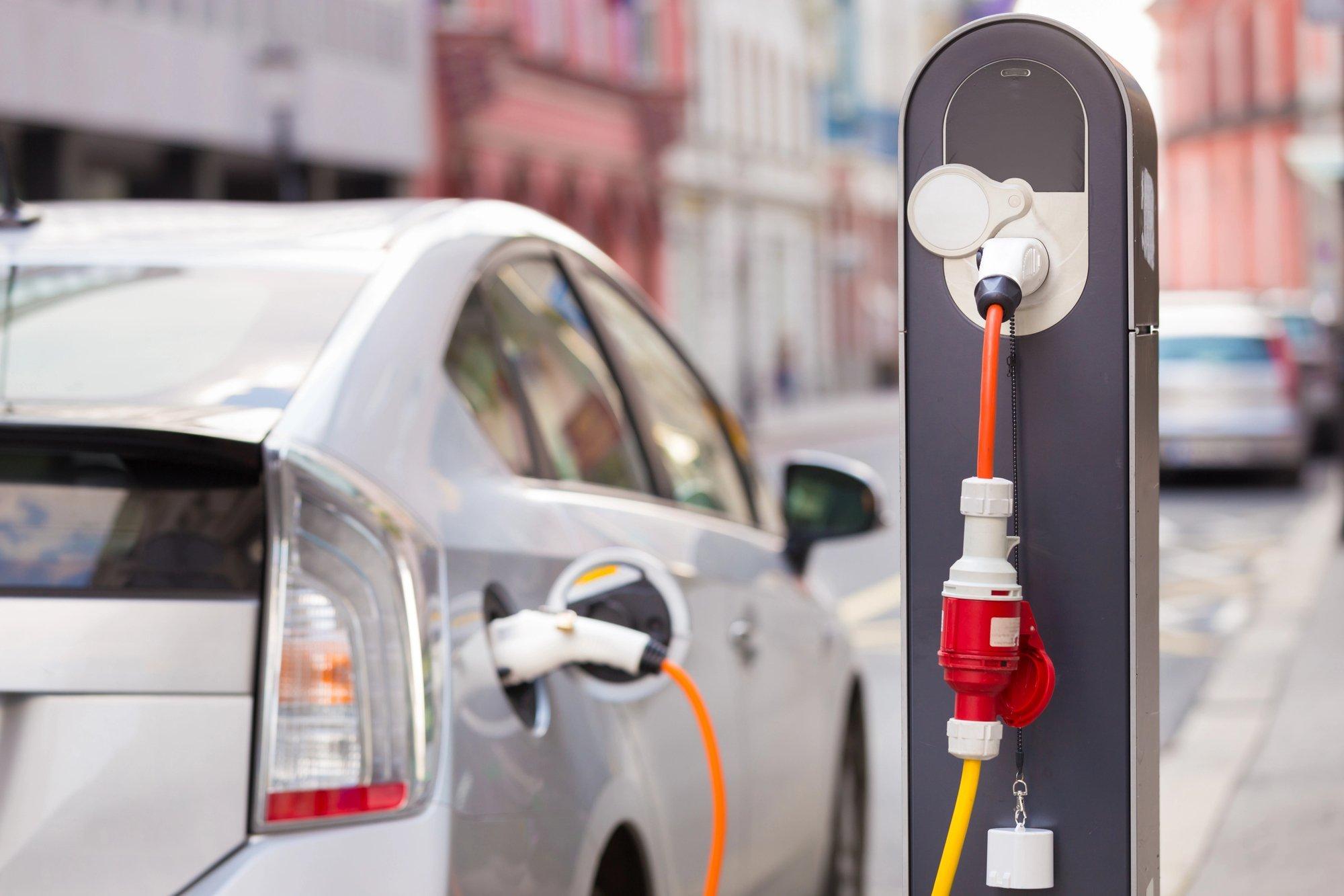 Weißes Elektroauto an der Ladesäule in einer Stadt.