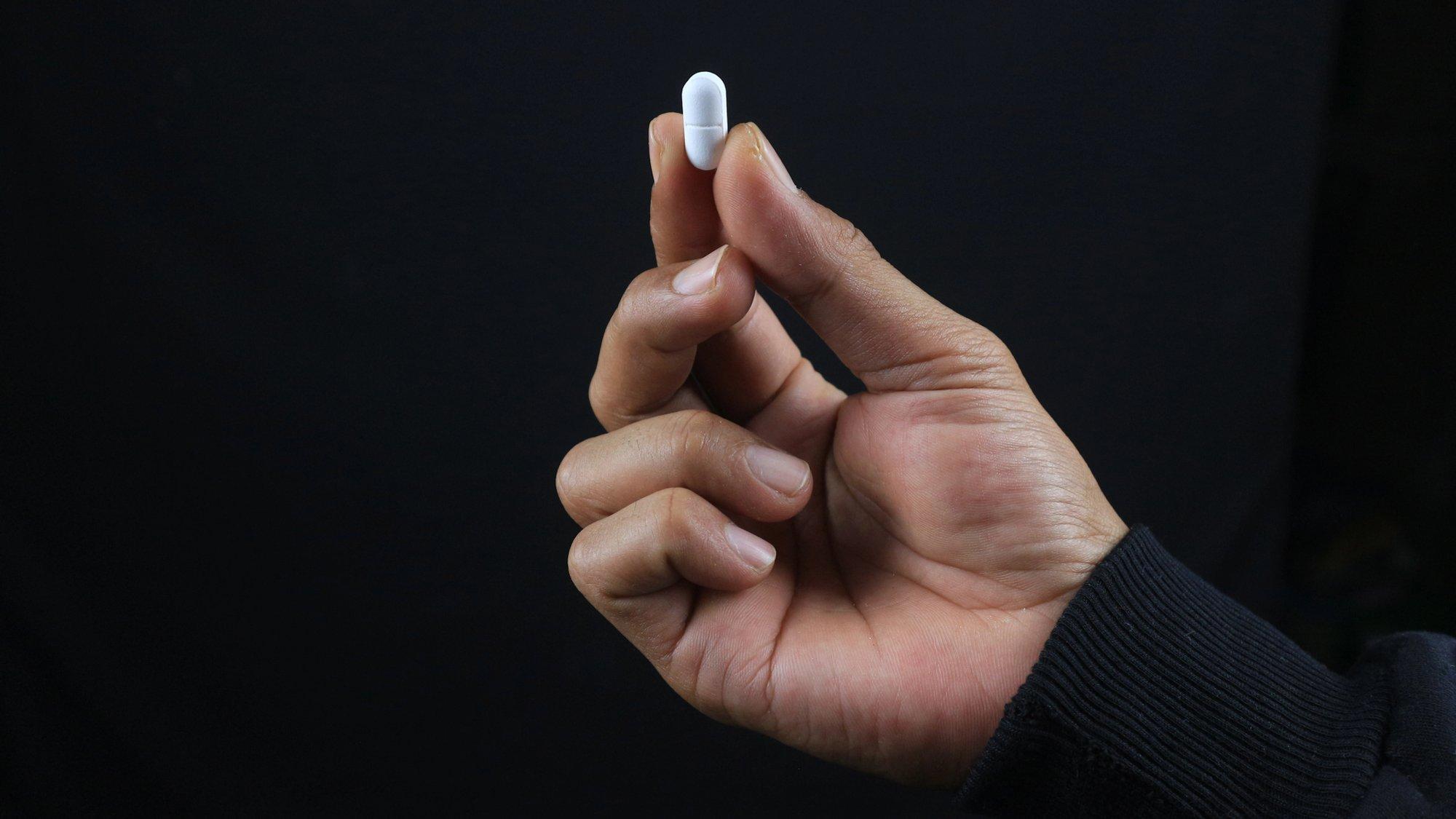 Hand vor schwarzem Hintergrund: Zeigefinger und Daumen halten Tablette in der Hand.