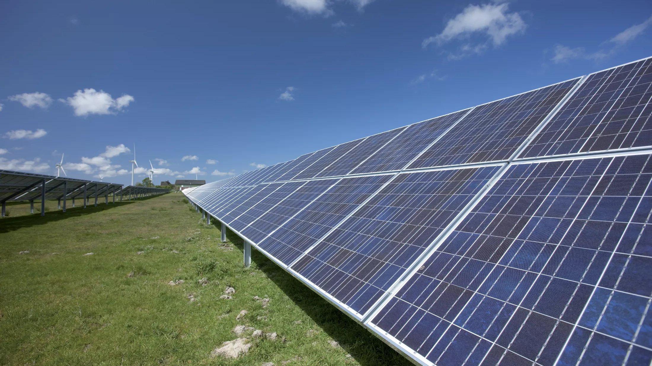 Lange Reihe von Photovoltaik-Modulen in einem Solarpark unter blauem Himmel