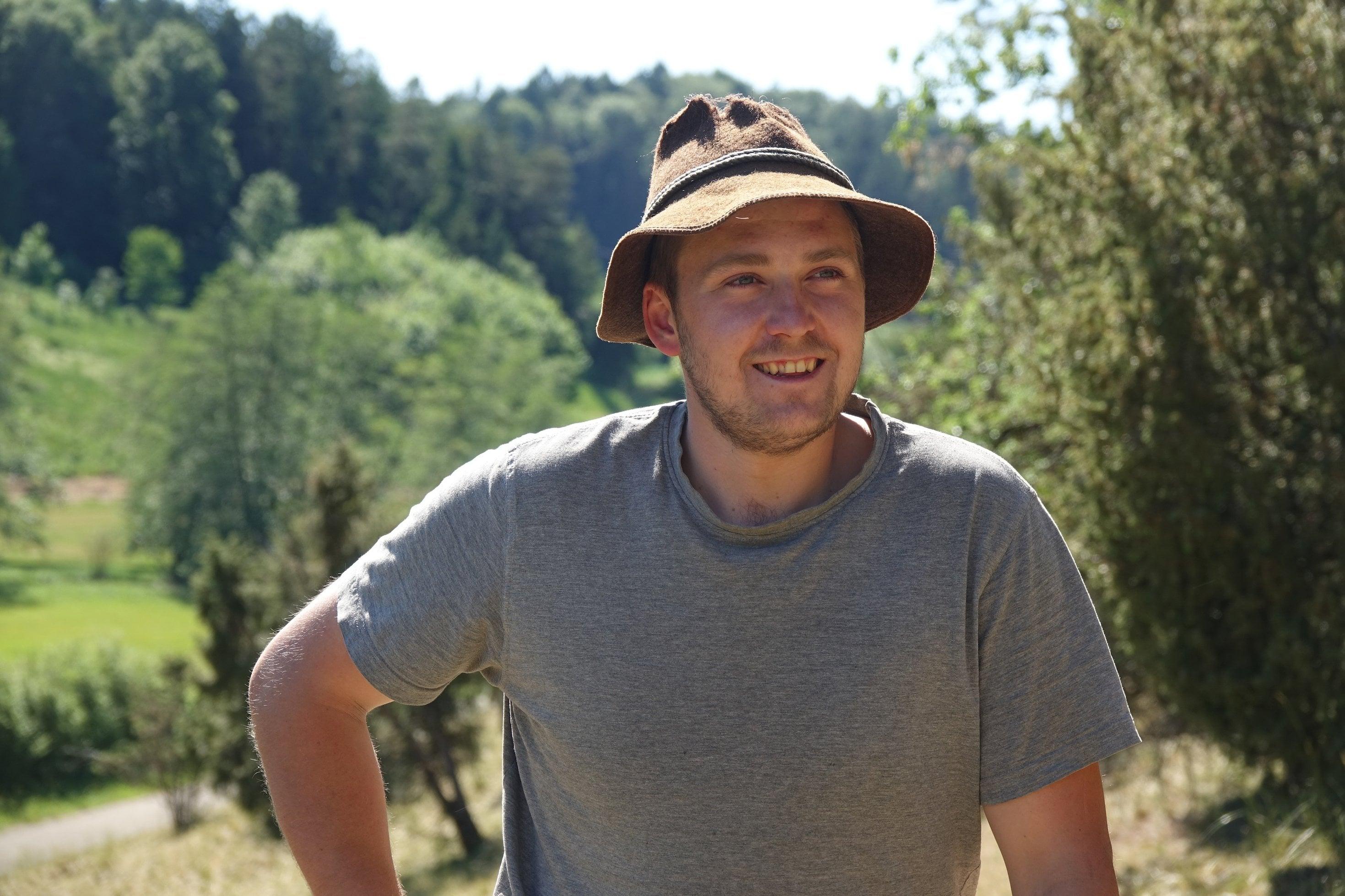 Junger Mann mit braunem Filzhut in Landschaft.