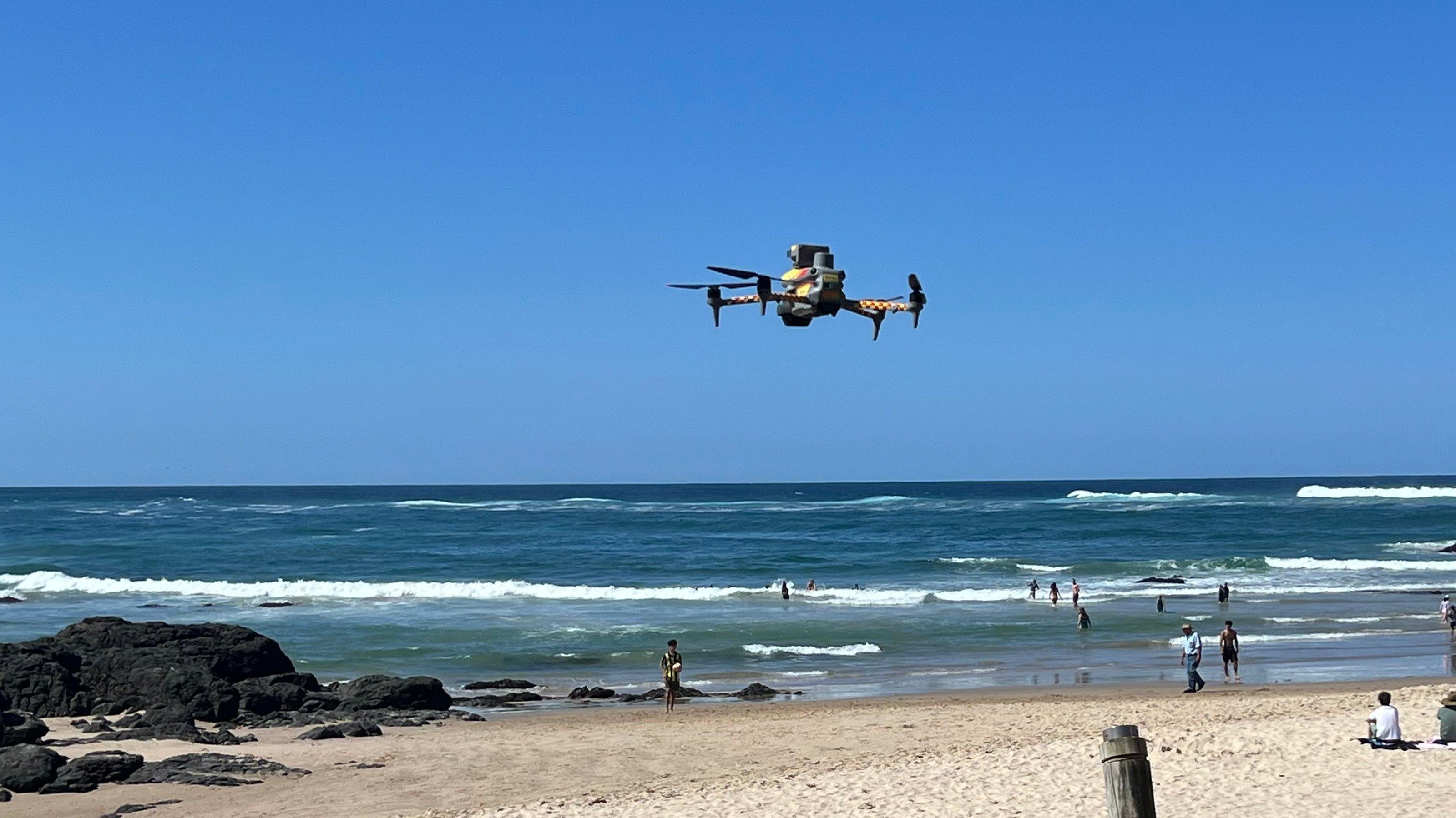 Eine Drohne fliegt über einem Strand, es ist der Town Beach von Port Macquarie, wo gerade eine Pilotin eine Drohne mit Kamera zu einem Überwachungsflug losgeschickt hat.
