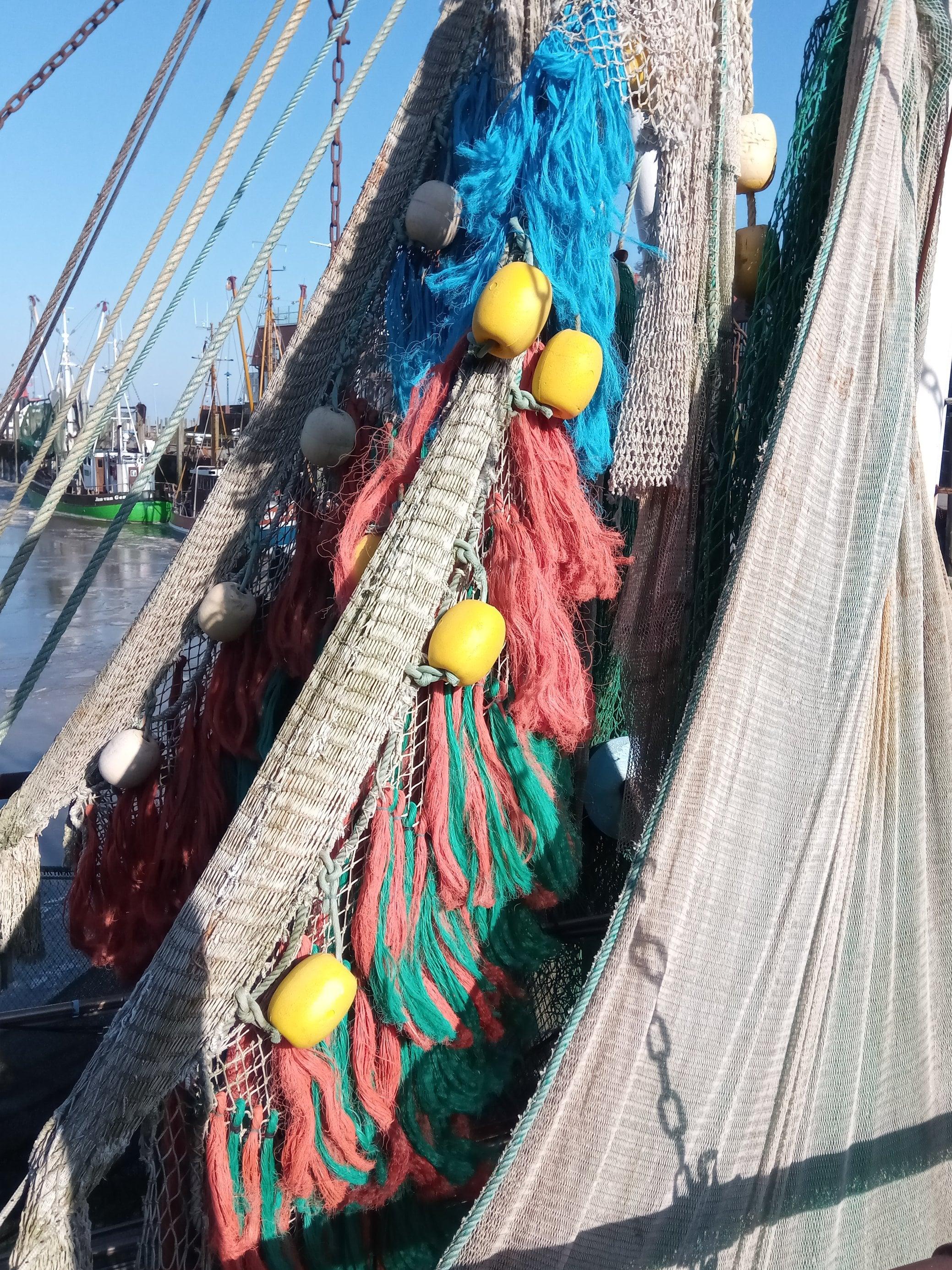 Foto zeigt hängende Netze mit Dolly Ropes in Orange und Blau an Deck eines Bootes. Sie sind keine Zierde, sondern ein schlecht durchdachtes Prinzip, um die Netze der Fischer zu schützen.