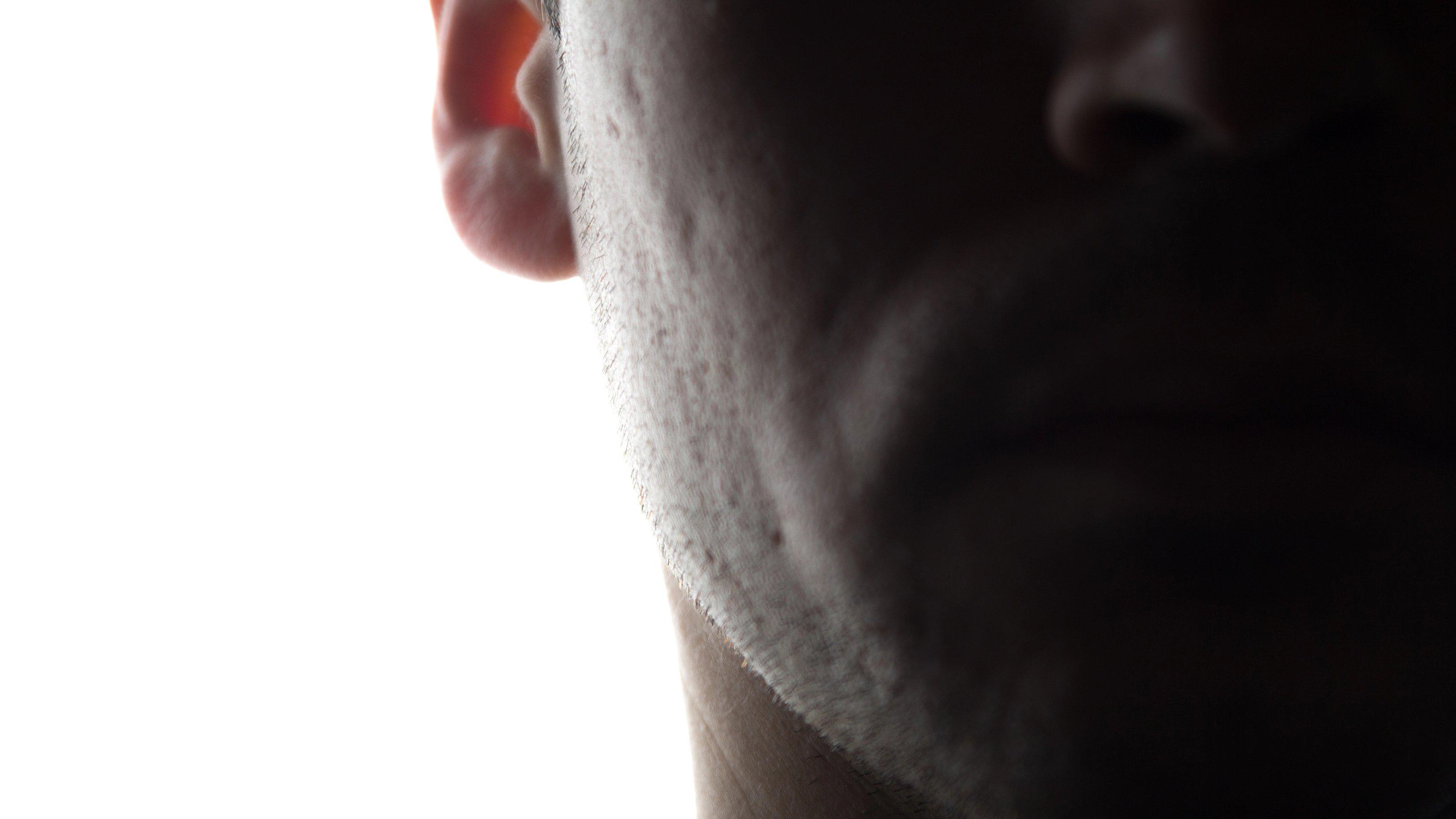 Der Ausschnitt der unteren rechten Gesichtspartie eines unbekannten Mannes im Schatten vor weißem Hintergrund.