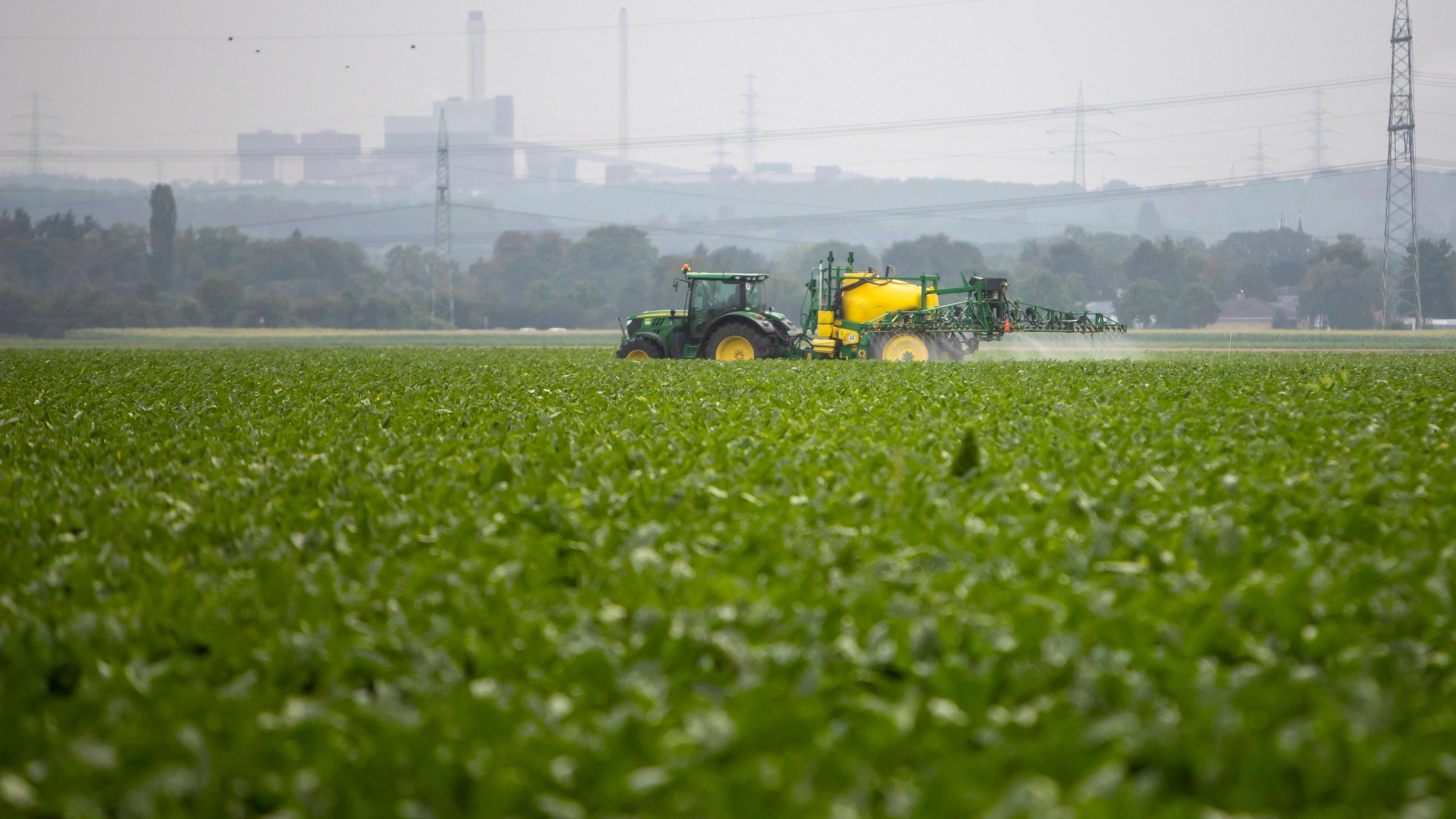 Traktor beim Spritzen, am Horizont Industrie
