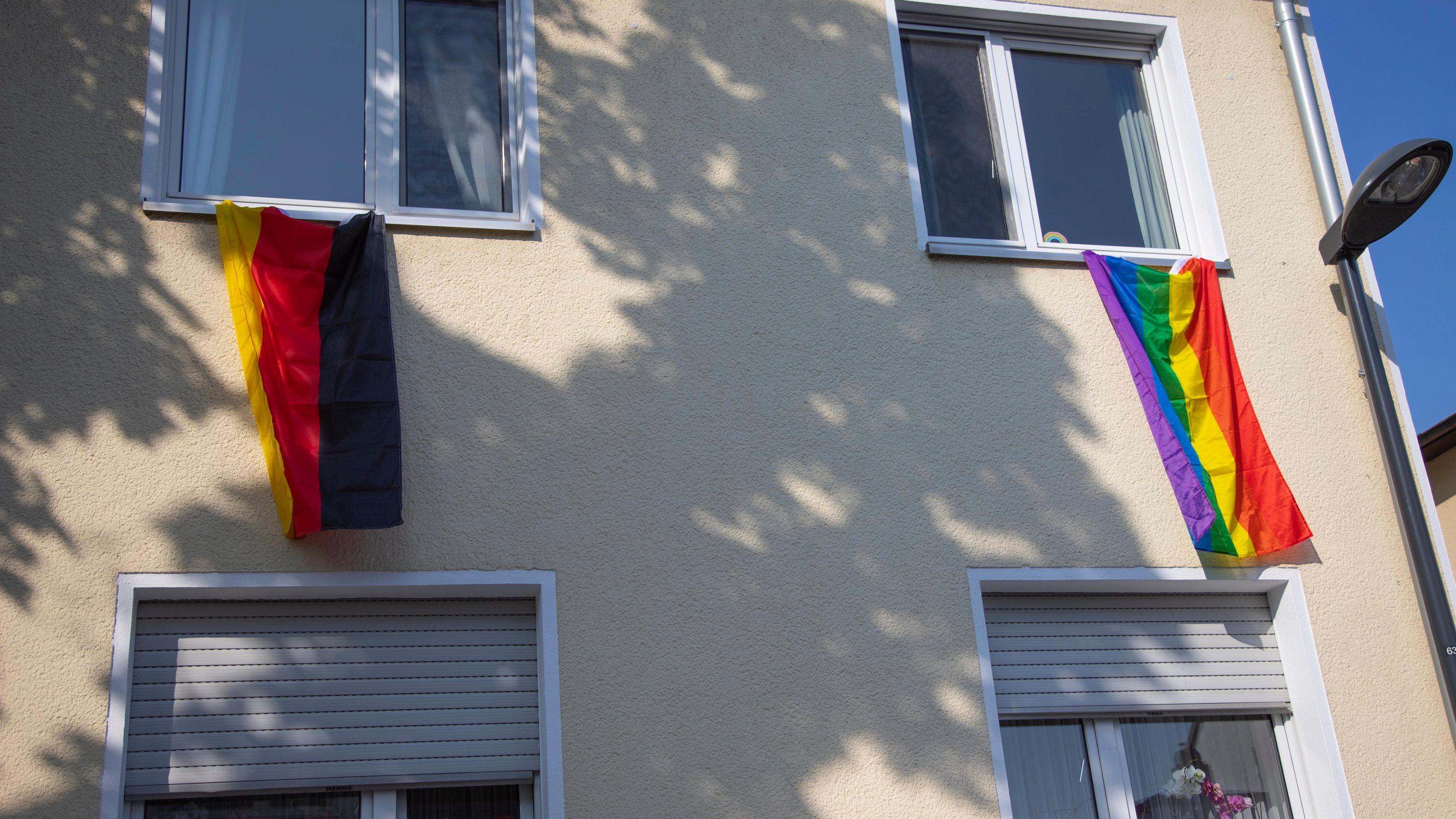 Eine Deutschland-Flagge und eine Pride-Flagge hängen an den Fenstern eines Wohnhauses