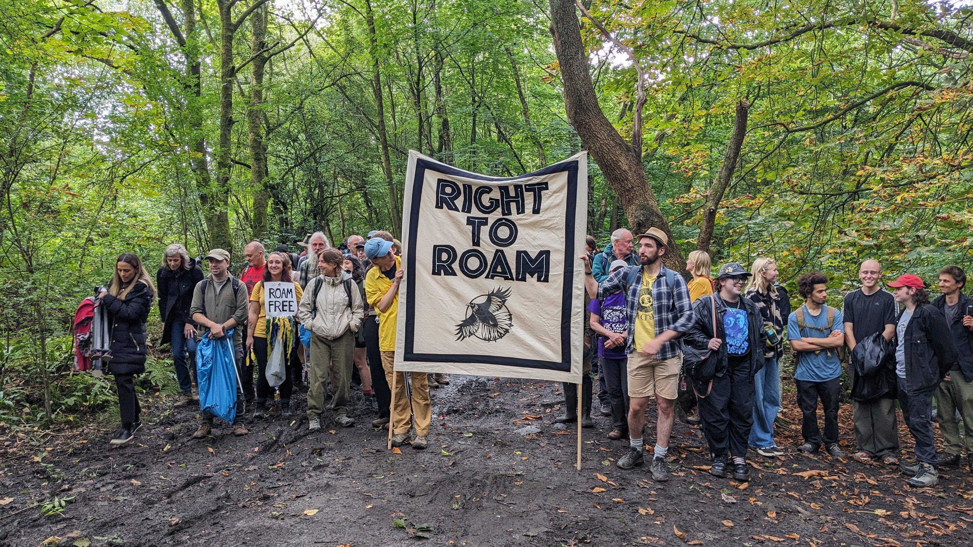 Eine Gruppe von Wanderer:innen, die mit einem großen Banner im Wald stehen. Auf dem Banner steht: Right to Roam.