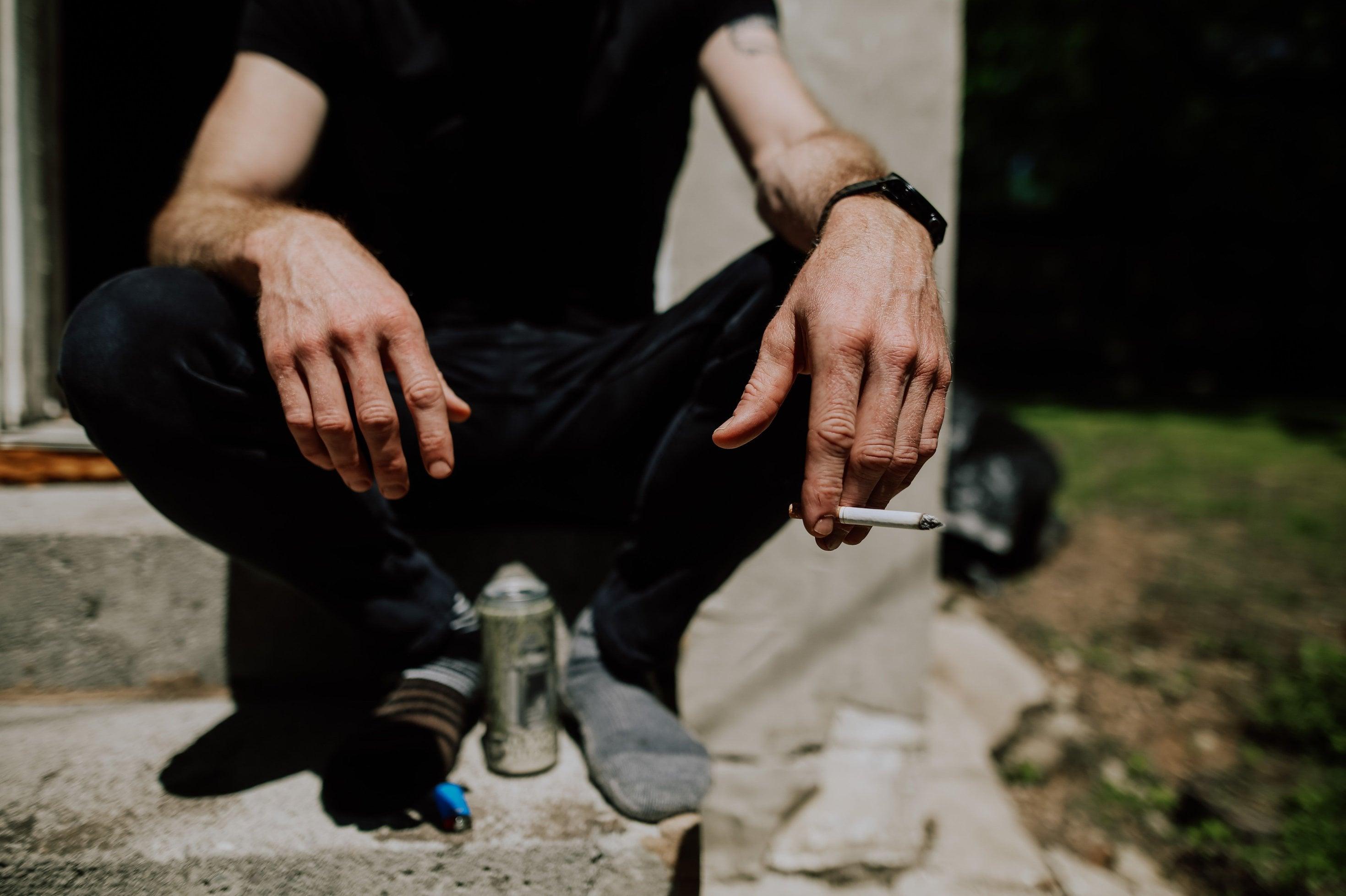 Ein Mann mit einer Zigarette in der Hand und einer Bierdose vor sich sitzt auf einer Treppe in einem Hauseingang.