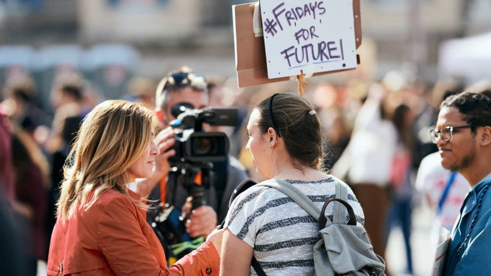 FridaysforFuture-Proteste in Rom. Eine Frau wird interviewt. Schild zeigt #FridaysforFuture.