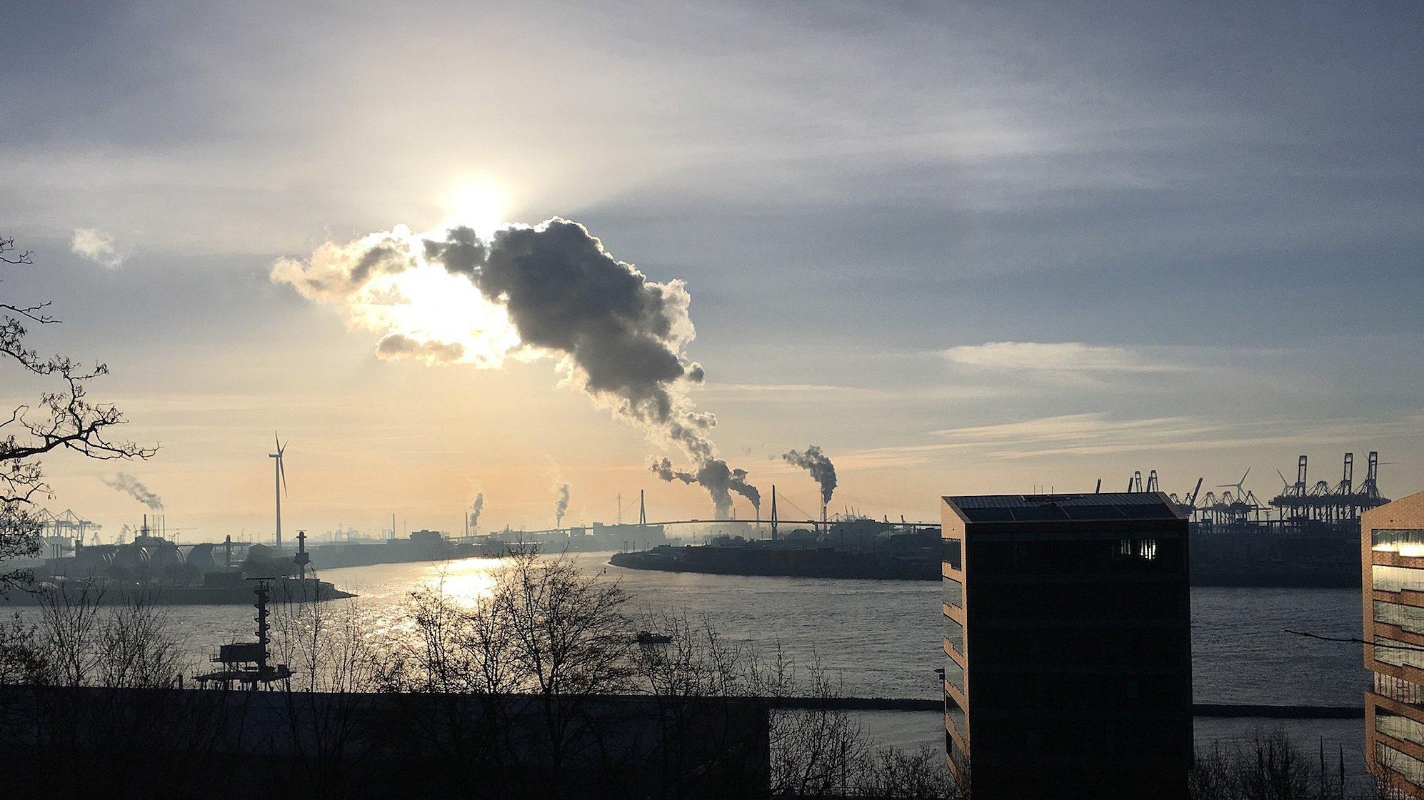 Bild vom Hamburger Elbufer im Stadtteil Altona: 
Vom Hochufer in Hamburg-Altona geht der Blick über die Elbe nach Süden. Dort hinter der Köhlbrandbrücke sind etliche Industriebetriebe angesiedelt, unter anderem das Kohlekraftwerk Moorburg. Die sichtbaren Wolken sind nur Wasserdampf, aber aus den gleichen Schornsteinen entweicht auch eine große Menge CO2.