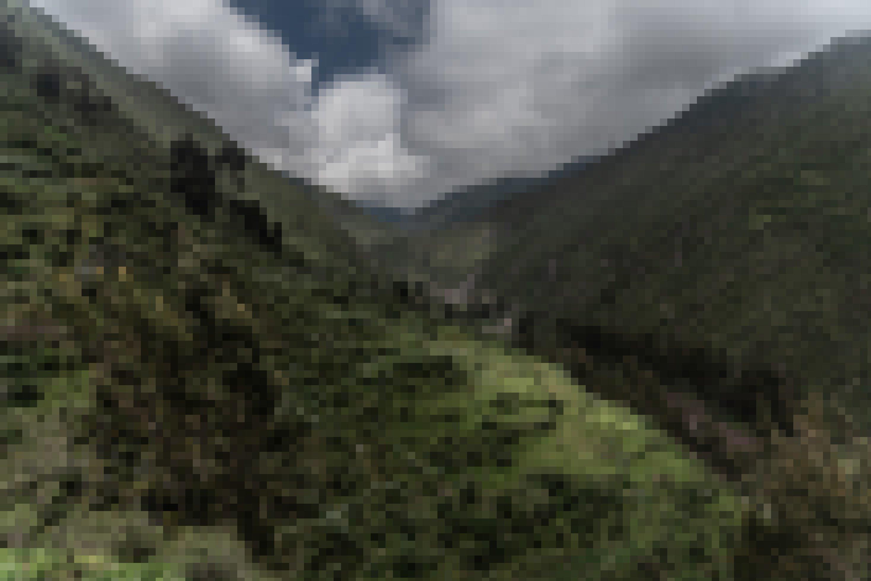 Unter stimmungsvollen Wolken zeigt sich eine steile, grün bewachsene Schlucht, durch die eine Straße führt.