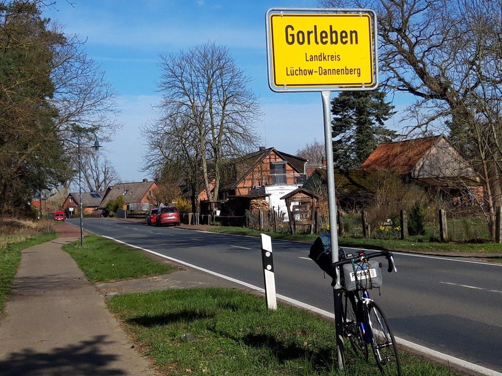 Das Rad des Autors lehnt am östlichen Ortsschuld von Gorleben; dahinter sind Häuser sowie die leere Dorfstraße zu erkennen, an der einige wenige Autos parken.
