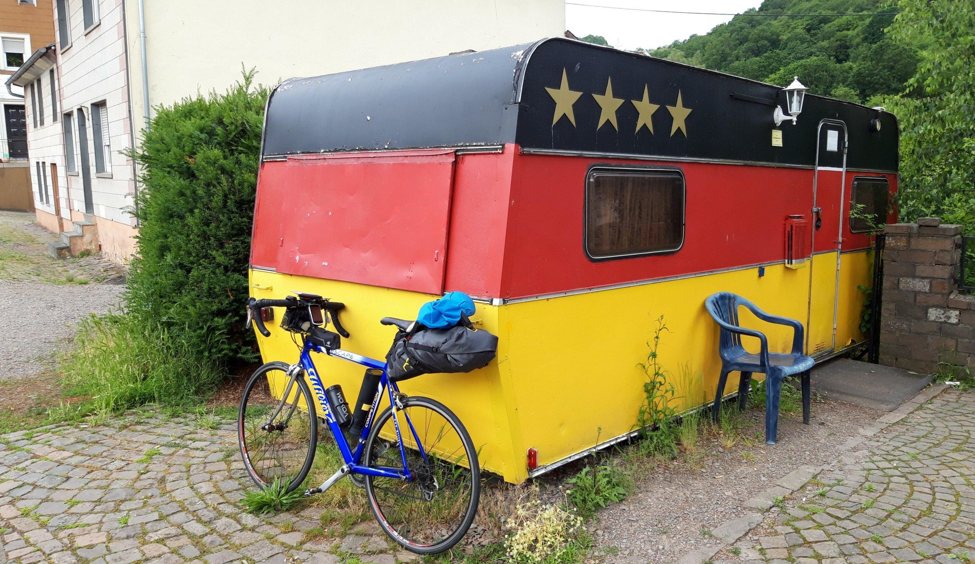 An der Dorfstraße von Rutsweiler steht ein betagter Wohnwagen, etwa zweimal so lang wie mein Fahrrad. Rundherum ist er schwarzrotgold gestrichen.
