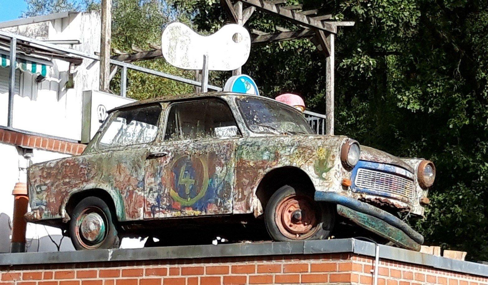 Besprühter Trabi, oben mit einer riesigen Schraube als Aufziehspielzeug dekoriert,