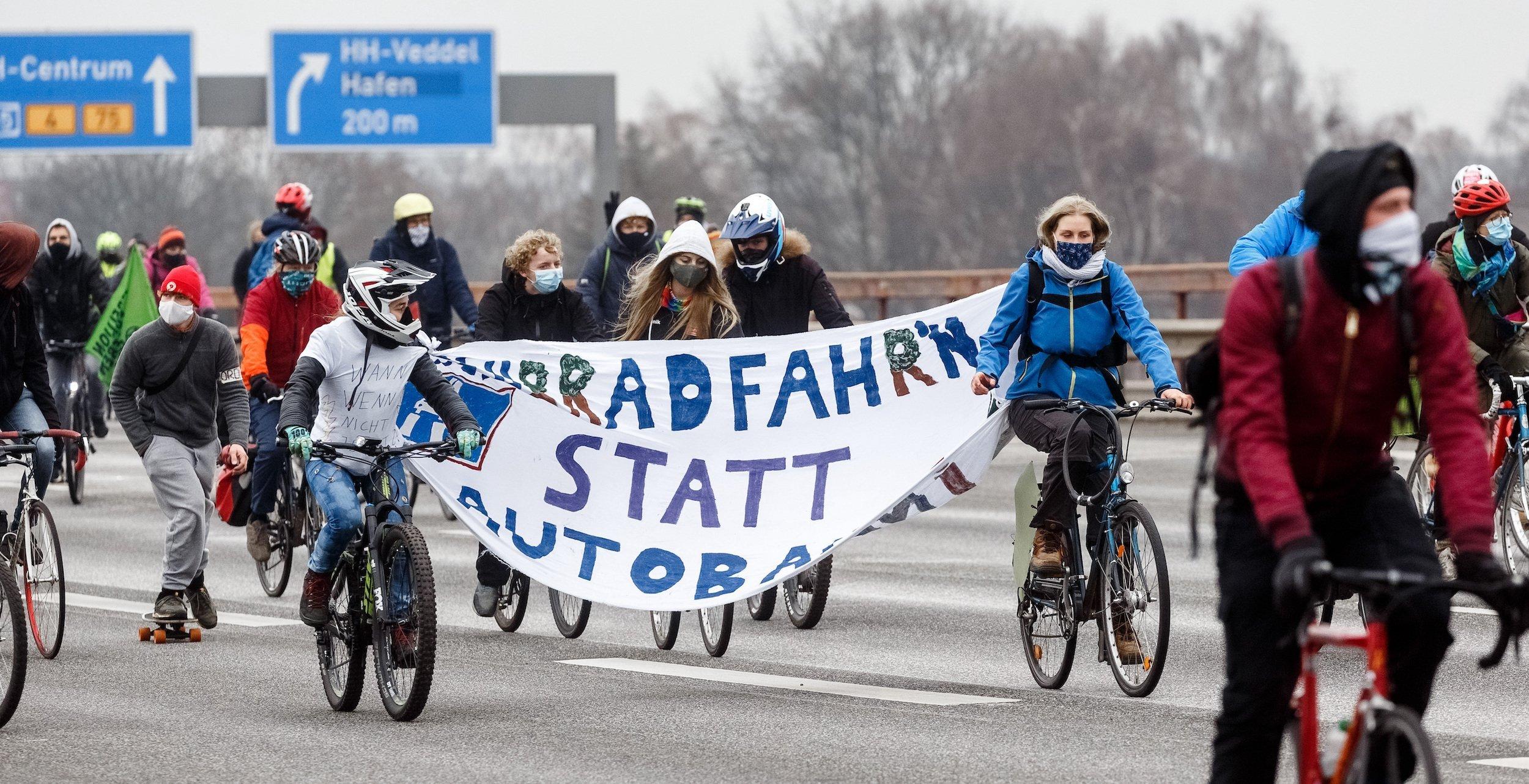Teilnehmer der Fahrrad-Demo radeln mit einem Banner mit der Aufschrift „Fahrradfahren statt Autobahn“ über die Autobahn.