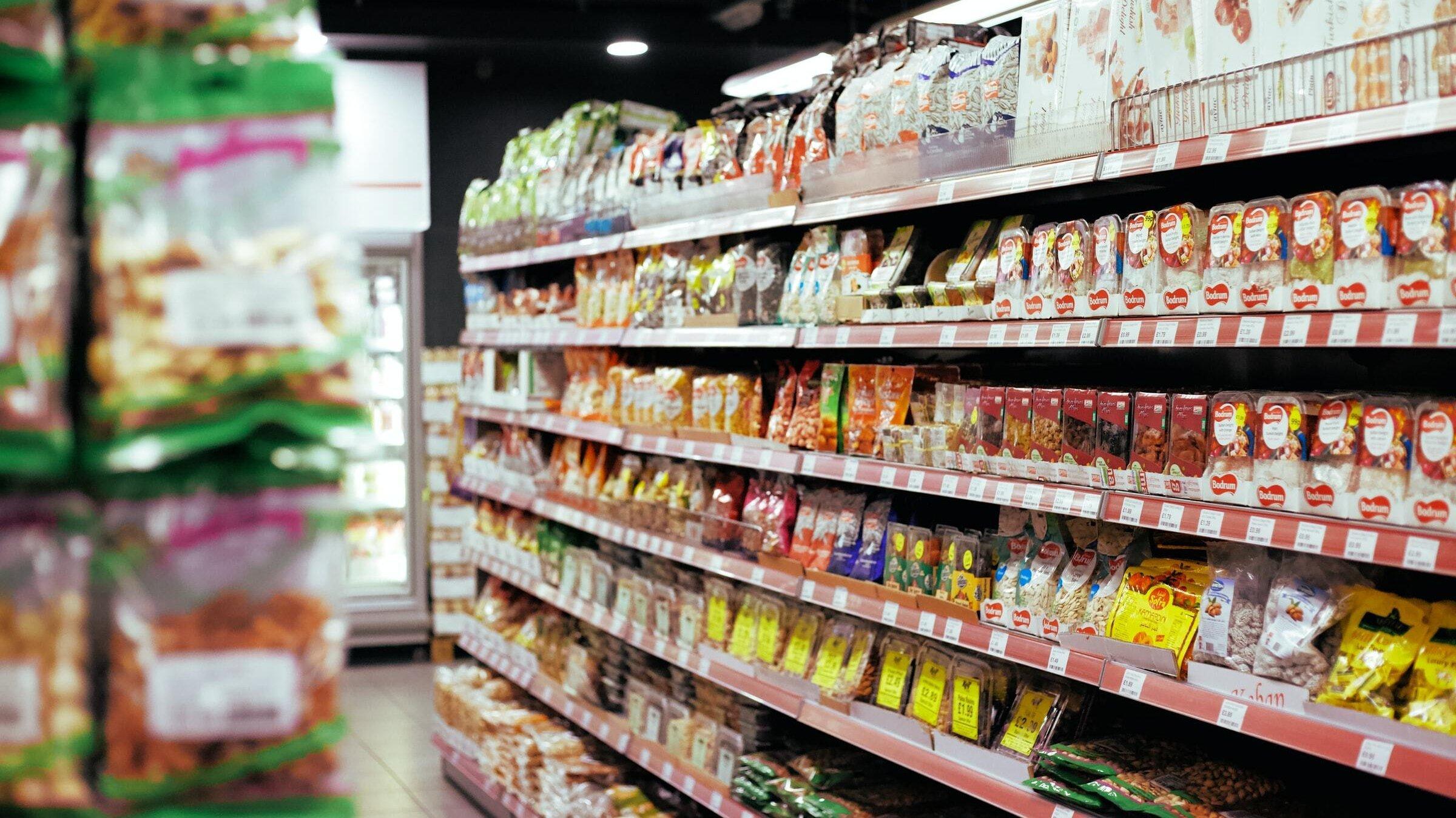 Viele bunte Lebensmittel-Verpackungen stehen in einem Regal in einem Supermarkt.