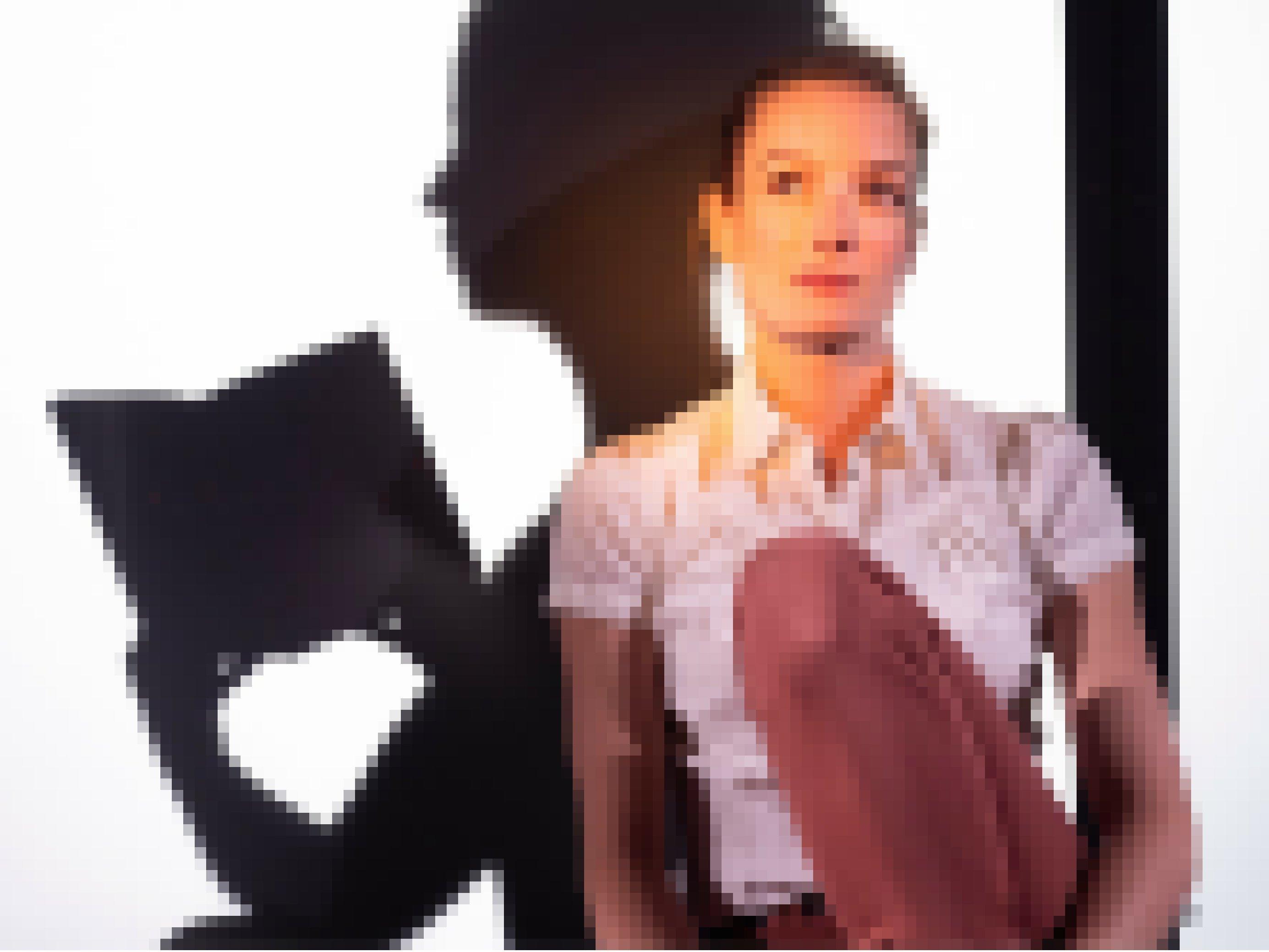 Eine junge Frau sitzt nachdenklich auf der Bühne vor einer weißen Wand. Hinter ihr ist ein Schatten, der in einem Buch liest. Das Bühnenbild von Ansgar Prüwer zeigt weitere Seiten von Anne.