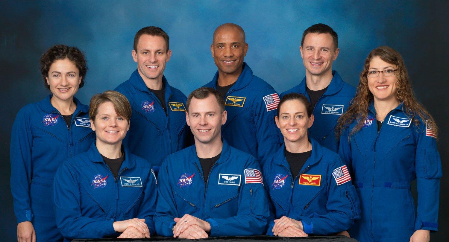 Die NASA-Astronautenklasse 2013 posiert vor blauer Leinwand: Anne McClain, Tyler „Nick“ Hague, Nicole Aunapu Mann, davor Jessica Meir, Josh Cassada, Victor Glover, Andrew „Drew“ Morgan und Christina Hammock (Koch)