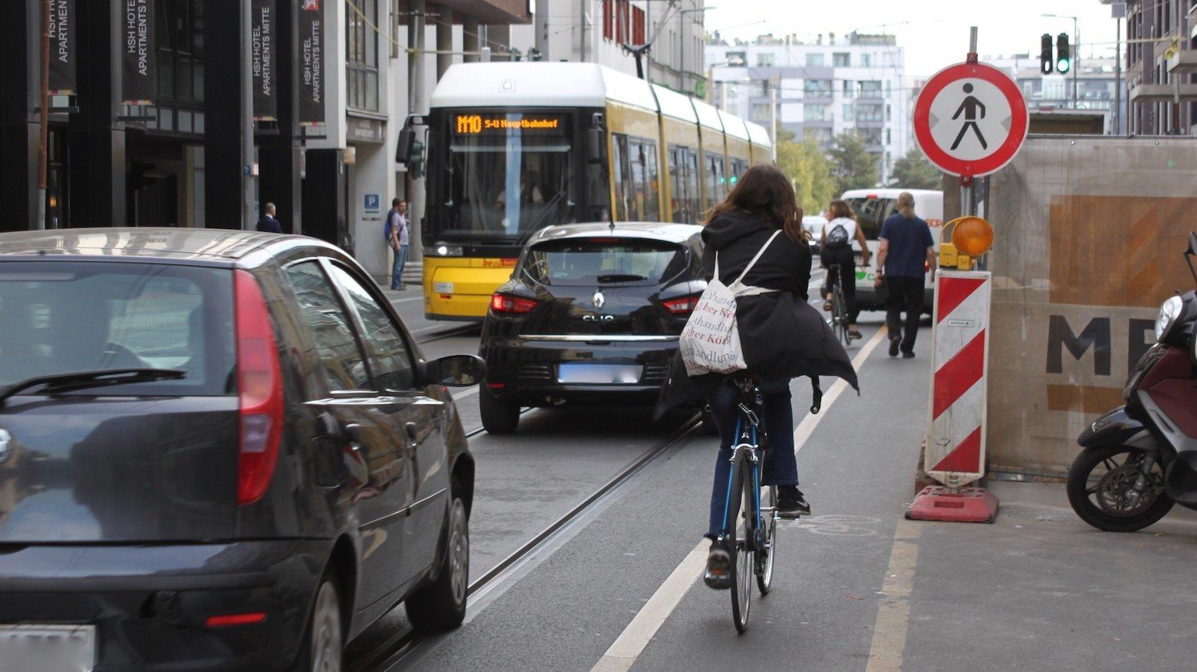 Eine befahrene Straße mit Baustelle. Ein Radfahrerin fährt an der Absperrung vorbei.