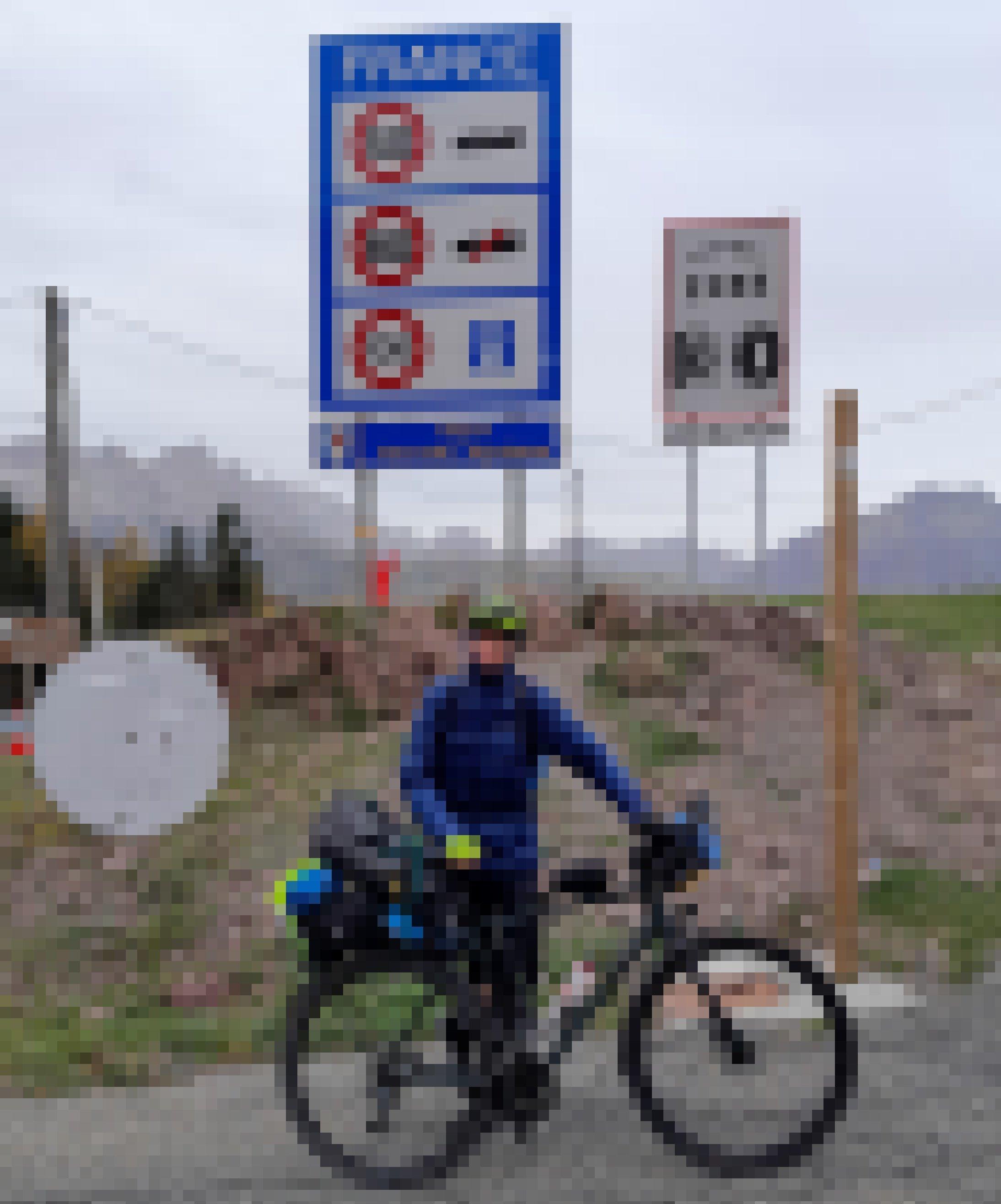 Der Reporter mit Daunenjacke und seinem Rennrad auf dem Alpenpass, dessen "Frankreich"-Landesschild den Beginn der Region "Nouvelle-Aquitaine" anzeigt