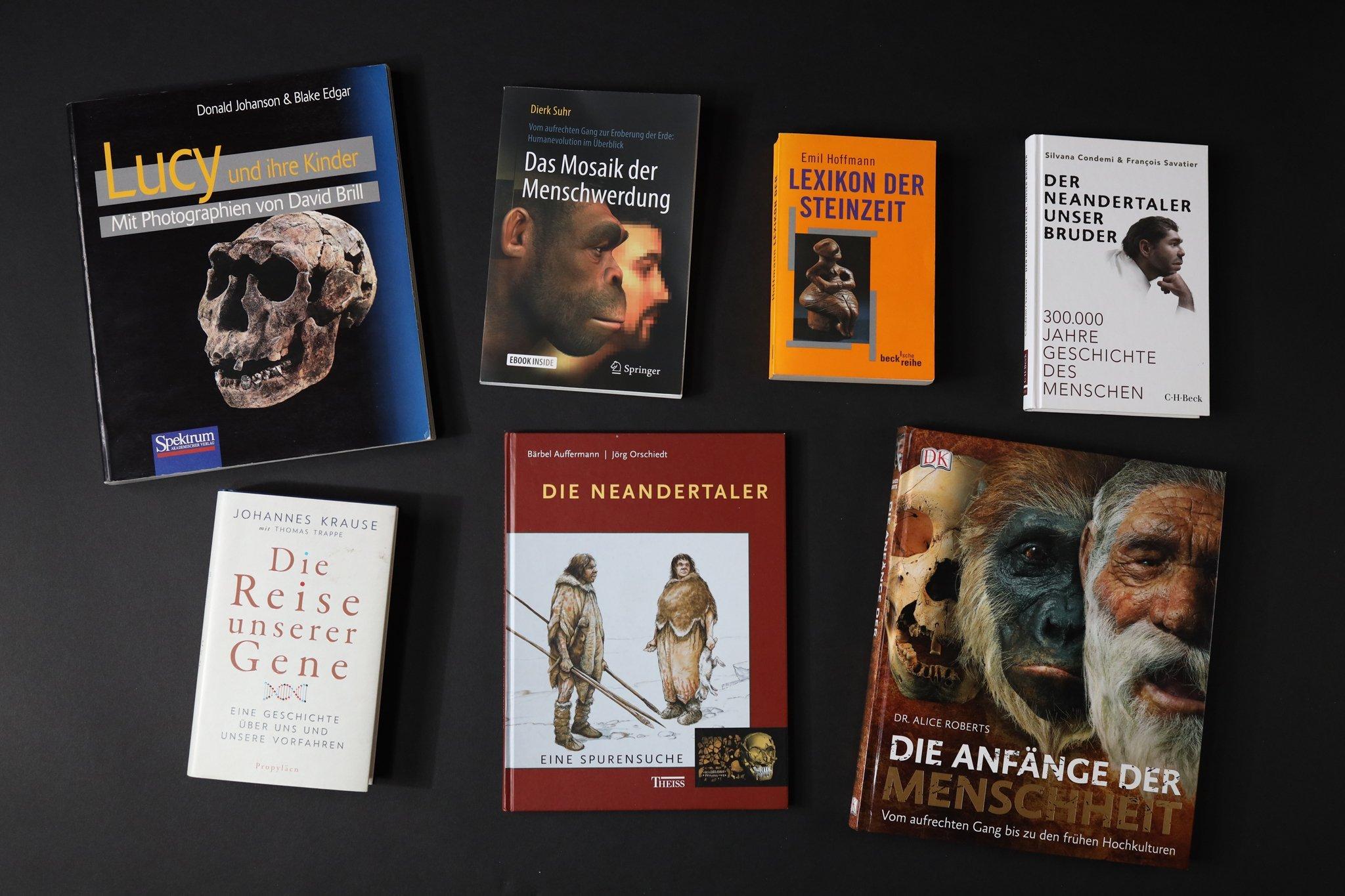 Auf diesem Foto sind die Cover von sieben Fachbüchern auf schwarzem Hintergrund zu sehen. Sie haben Titel wie „Lucy und ihre Kinder“, „Der Neandertaler, unser Bruder“, „Die Reise unserer Gene“ oder „Das Mosaik der Menschwerdung“.