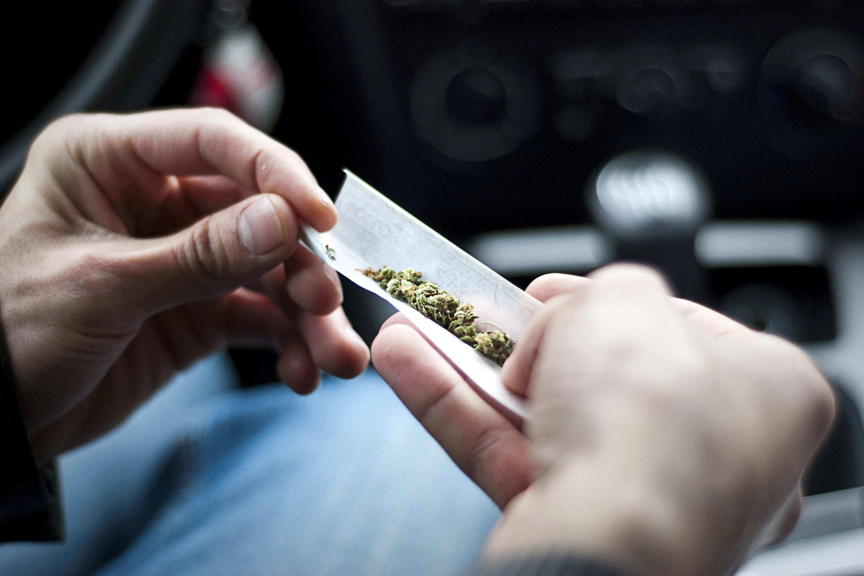 Das Foto zeigt zwei Hände, die ein ein Blättchen mit Cannabis/Gras halten, um einen Joint zu drehen.