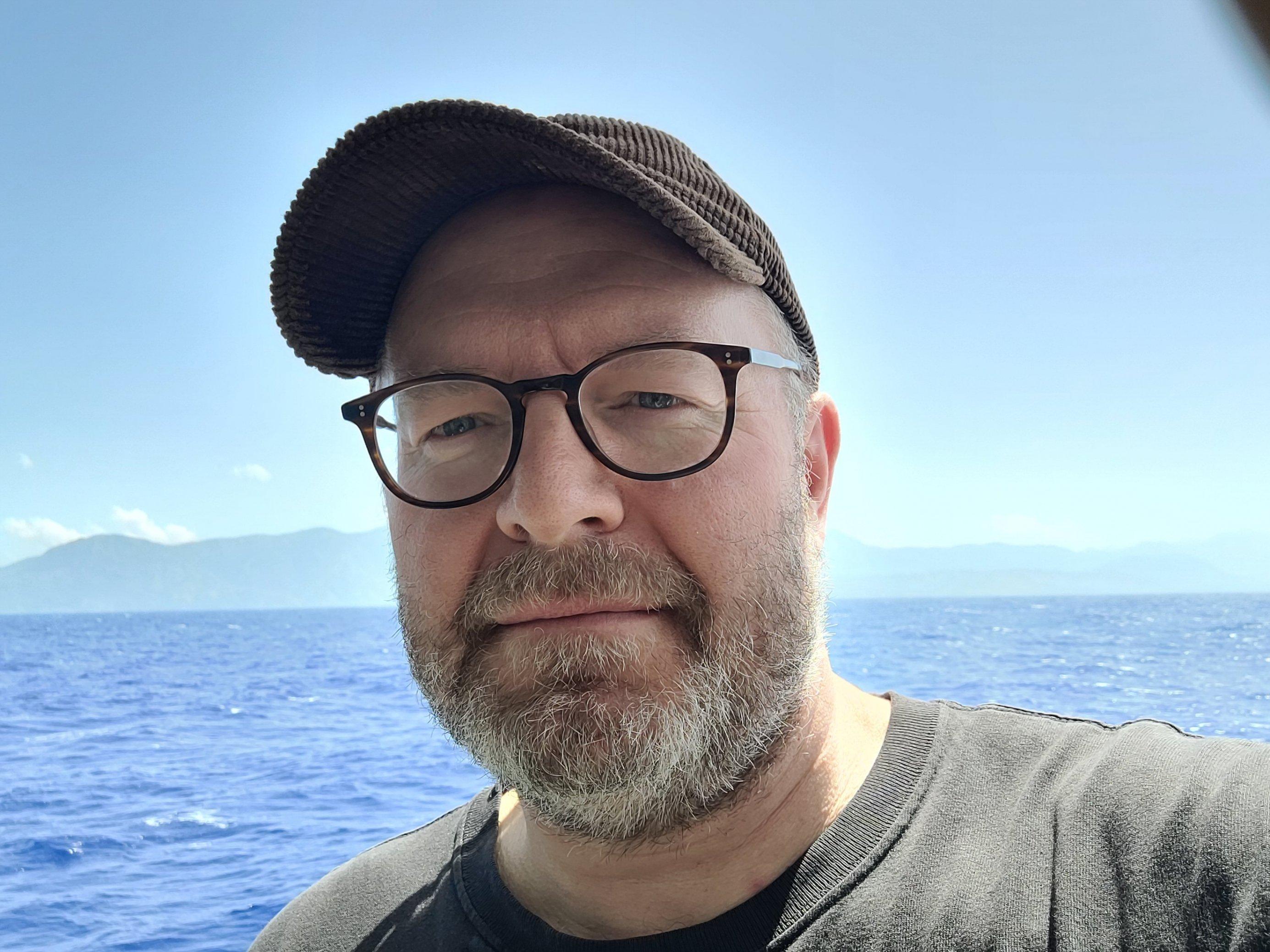 Mann mit Brille und Schirmmütze im Hintergrund Meer