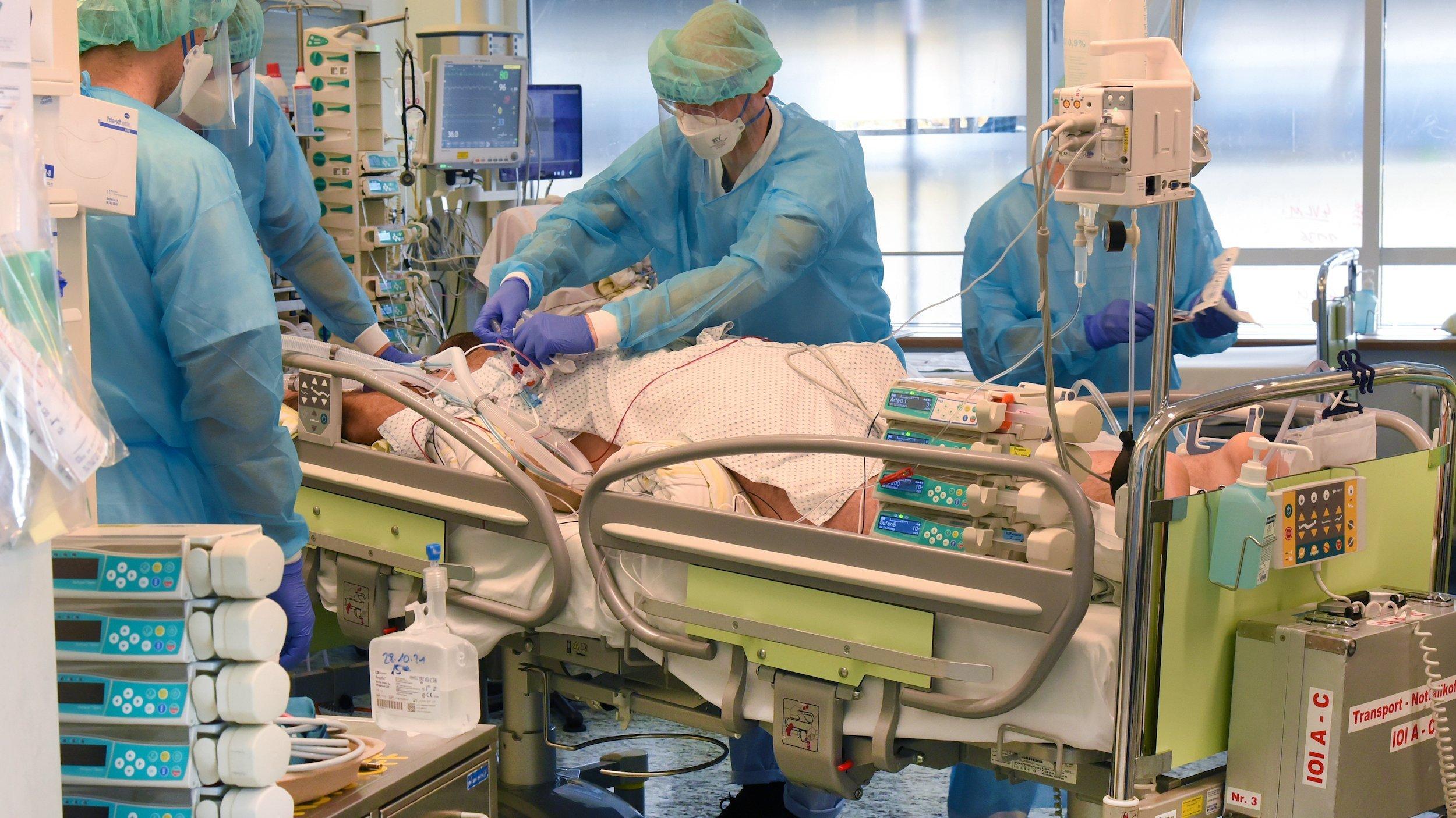 Ein medizinisches Team in Schutzkleidung ist inmitten von medizinischem Gerät um den auf dem Bauch liegenden Patienten versammelt.