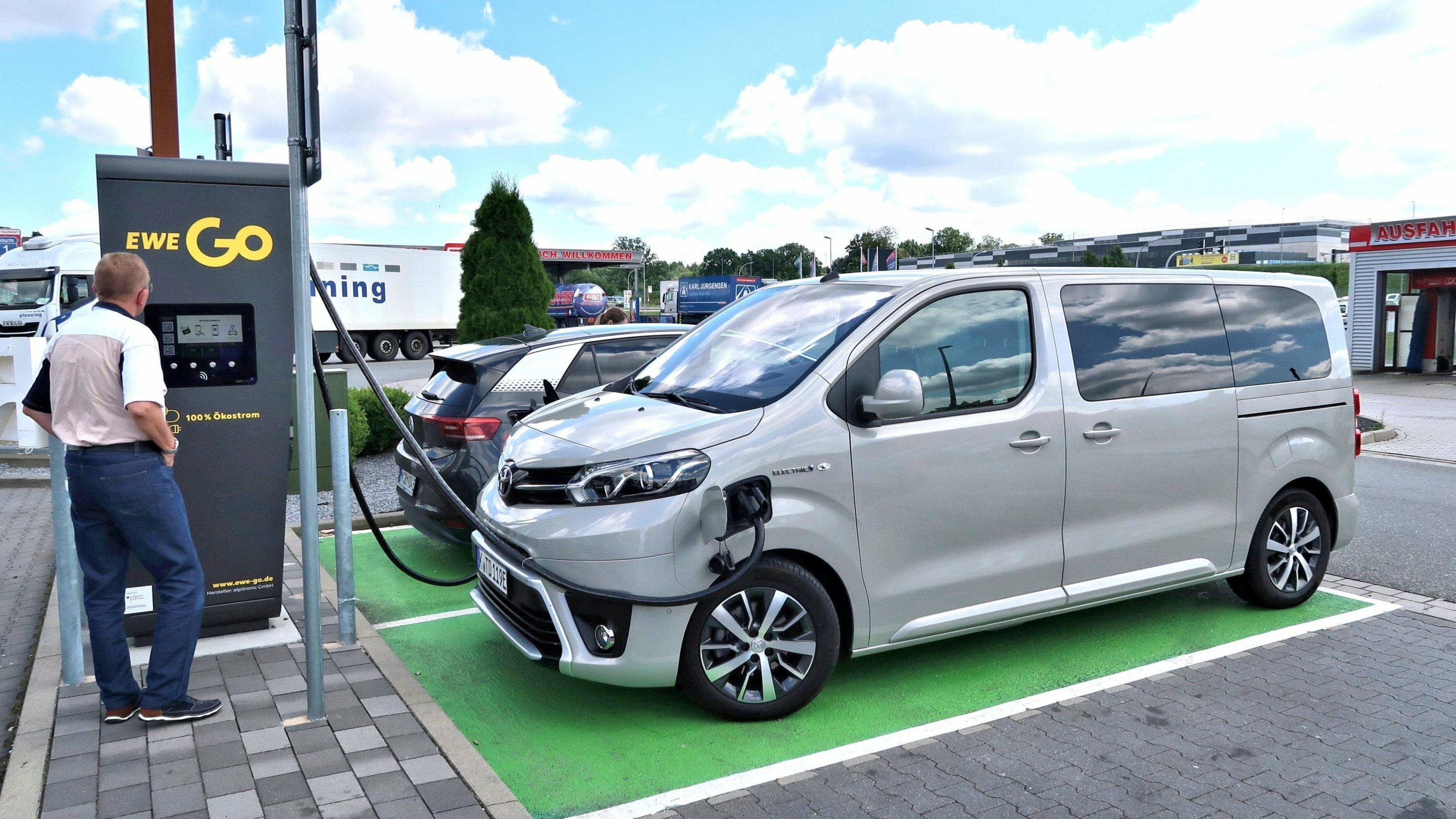 Ein elektrische Transporter ist an eine Schnellladesäule von EWE angeschlossen, davor steht ein Mann.