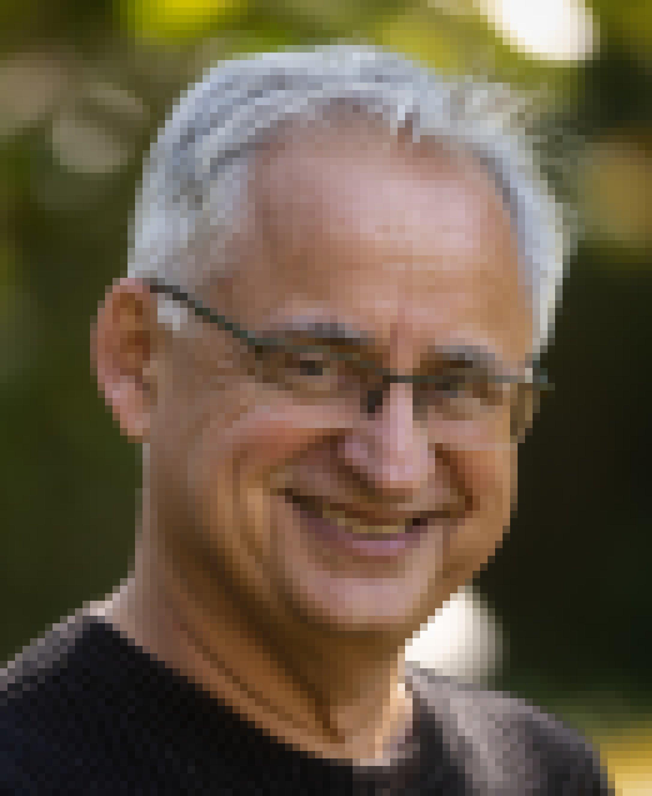 Ein Mann mit weißen Haaren und Brille lächelt in die Kamera