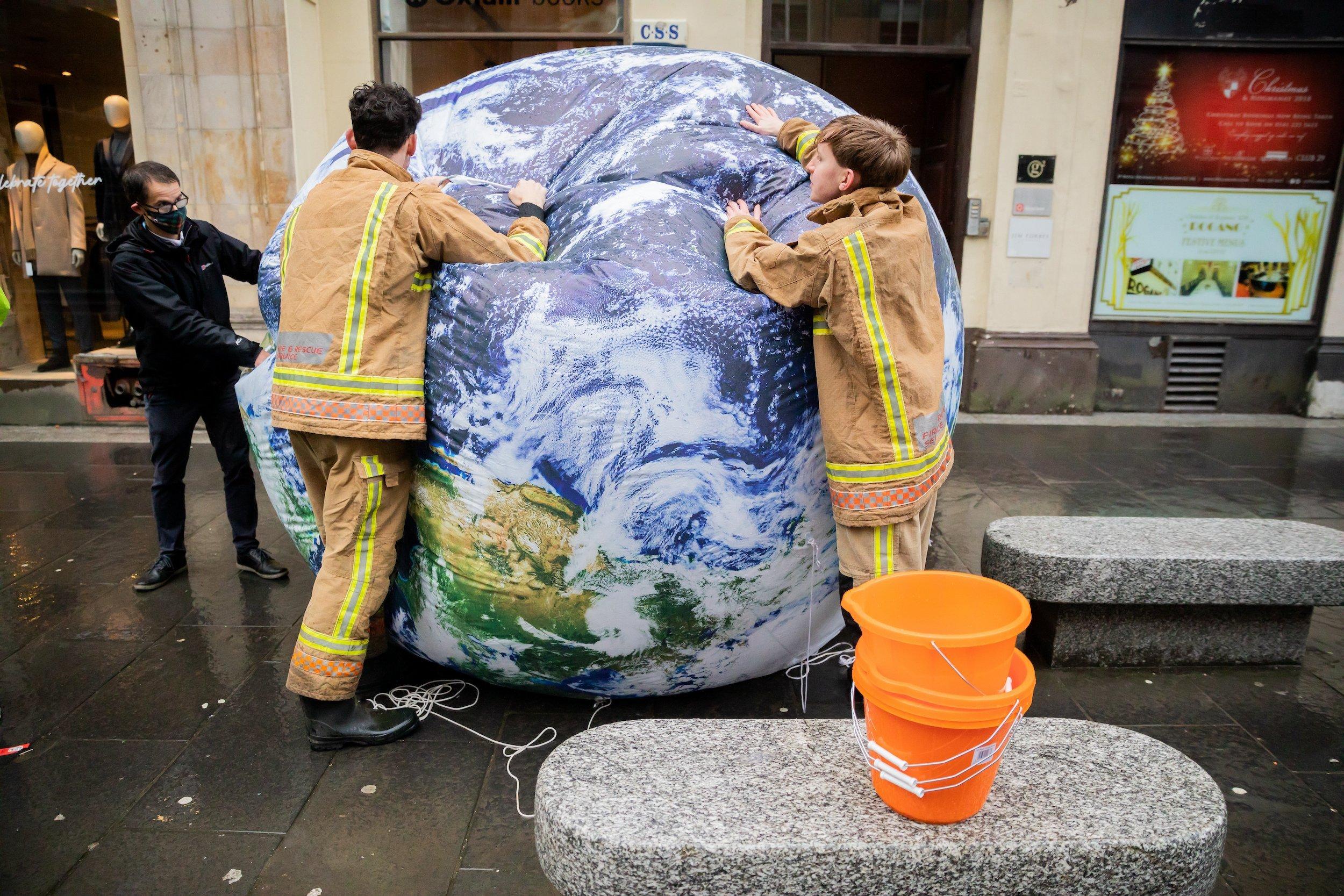 Aktivisten in Feuerwehrkostümen lassen nach einer Protestaktion von Oxfam die Luft aus einem Globus.