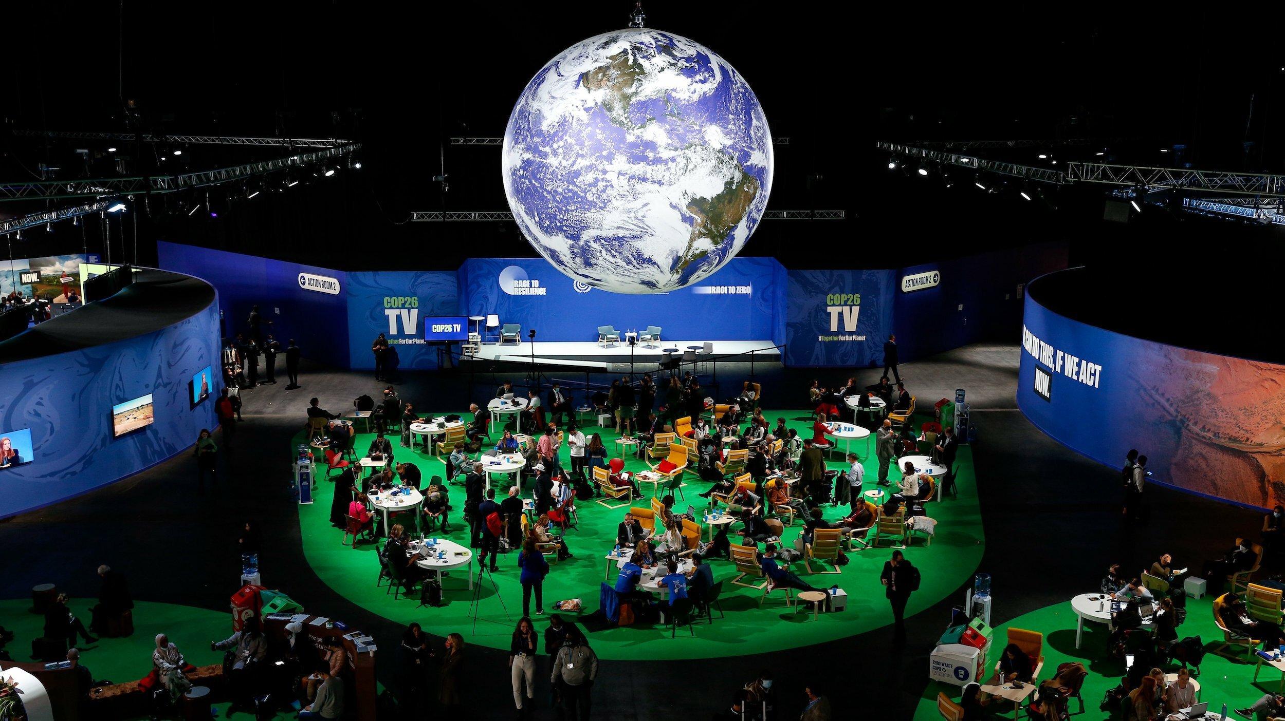 Inneres der Konferenzhalle, Menschen sitzen unter einem großen leuchtenden Modell der Erde.