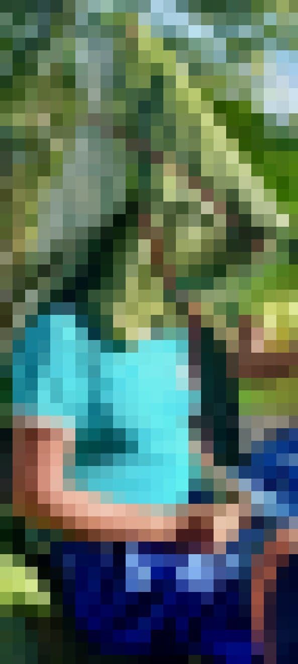Eine Frau sitzt im Bild. Ihr Kopf ist komplett in große, grüne Blätter eingeschnürt.