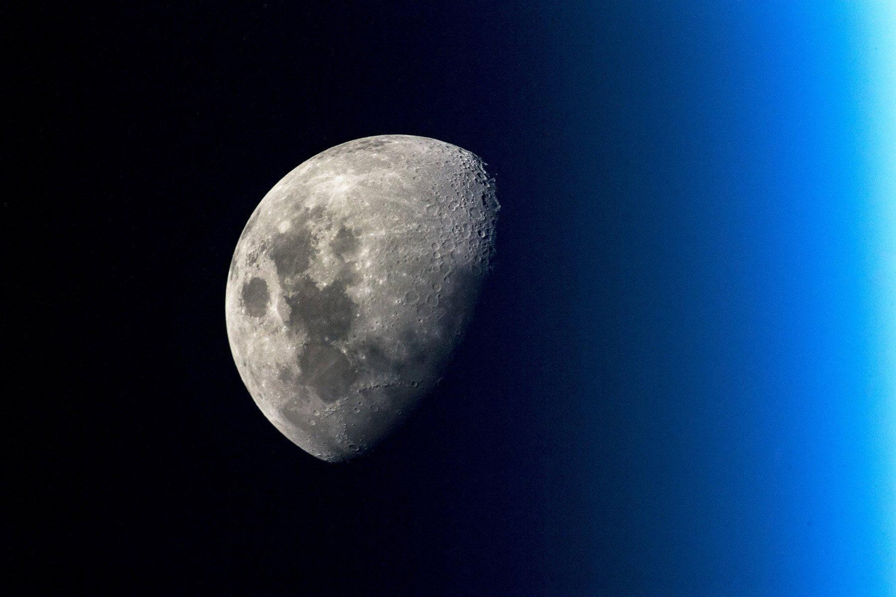 Der Mond vom Erdorbit aus fotografiert, im Vordergrund die blaue Erdatmosphäre.