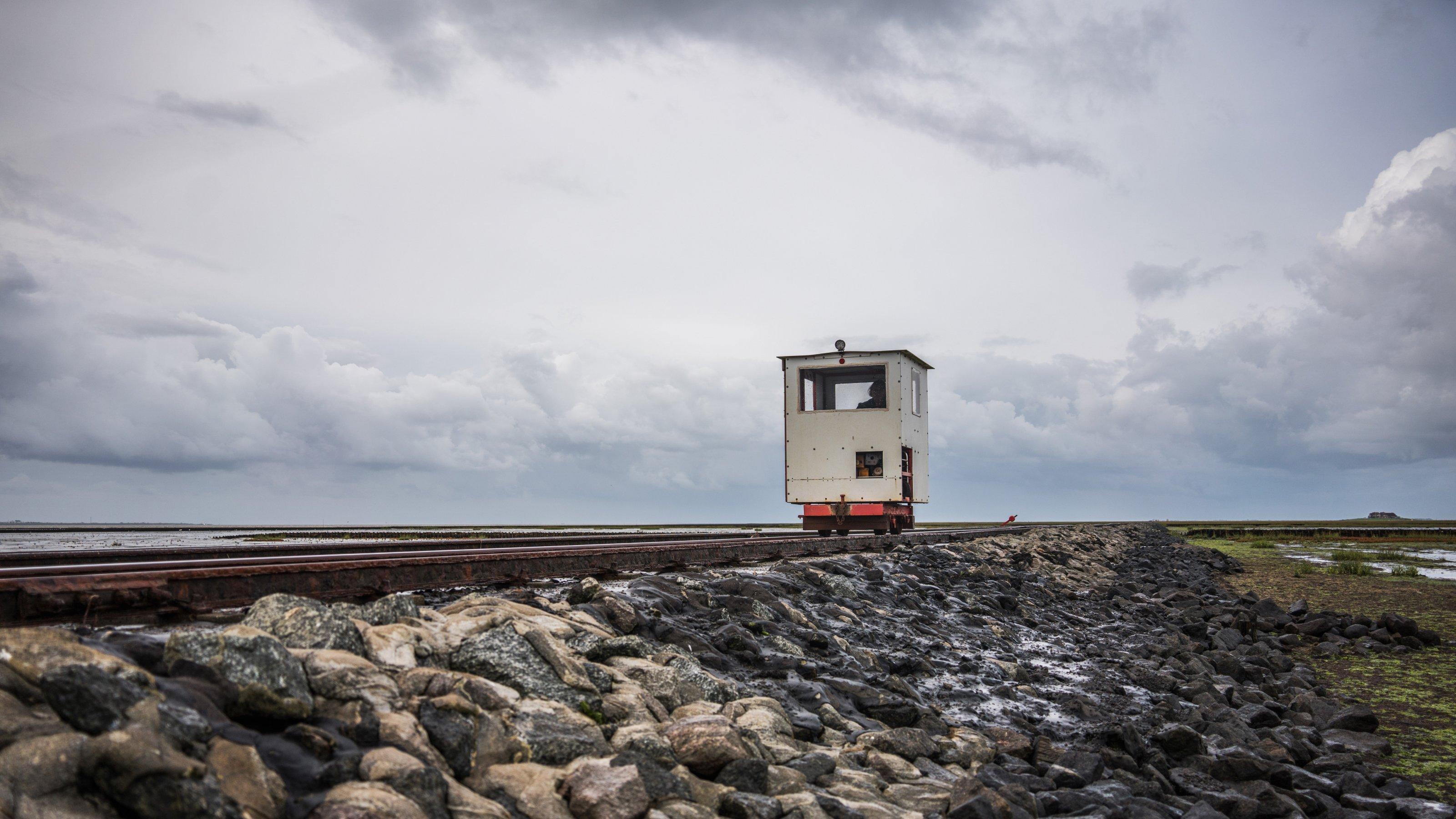 Eine Lore fährt über einen Damm durchs Wattenmeer