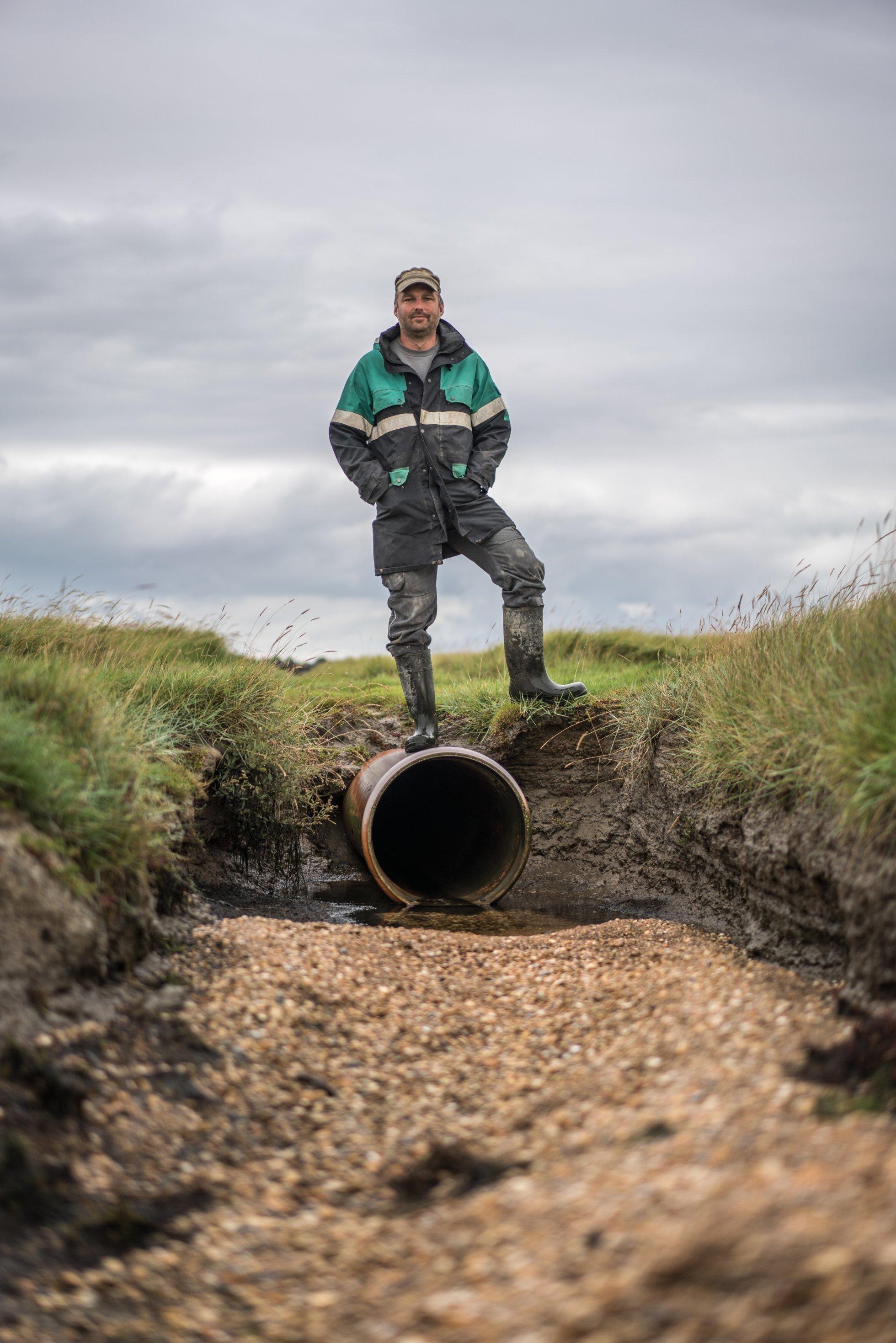 Mann steht auf einem Rohr, das in einer Salzwiese verlegt ist