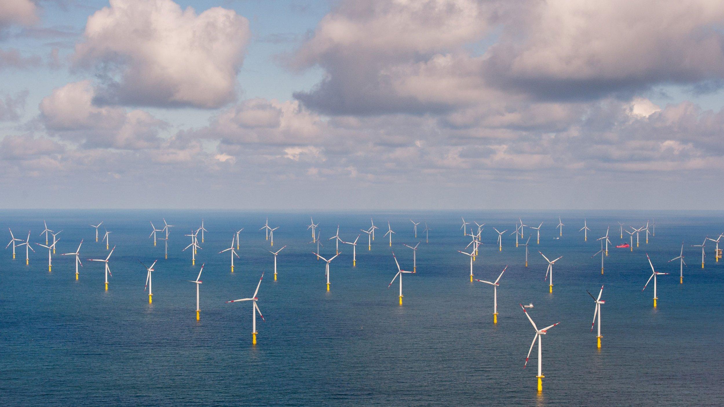 Zahlreiche Windkraftanlagen im Meer unter wolkigem Himmel.