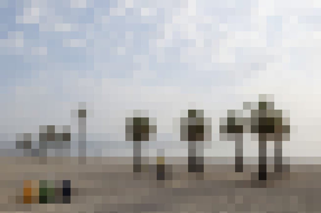 Der einsame Radfahrer schiebt sein Rad auf Holzplanken über den morgendlich erhellten Strand zum Meer.