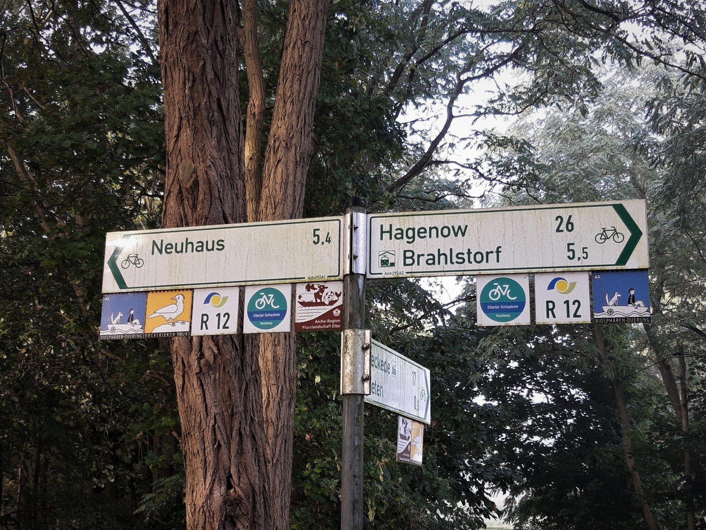 Radwege-Hinweisschilder nach Neuhaus und Brahlstorf, unterlegt mit Logos und Bezeichnungen fünf verschiedener Themenrouten: Biosphären-Querung, Vogelkieker-Tour, R12, Elbetal-Schaalsee-Radweg sowie Arche-Region Flusslandschaft Elbe.
