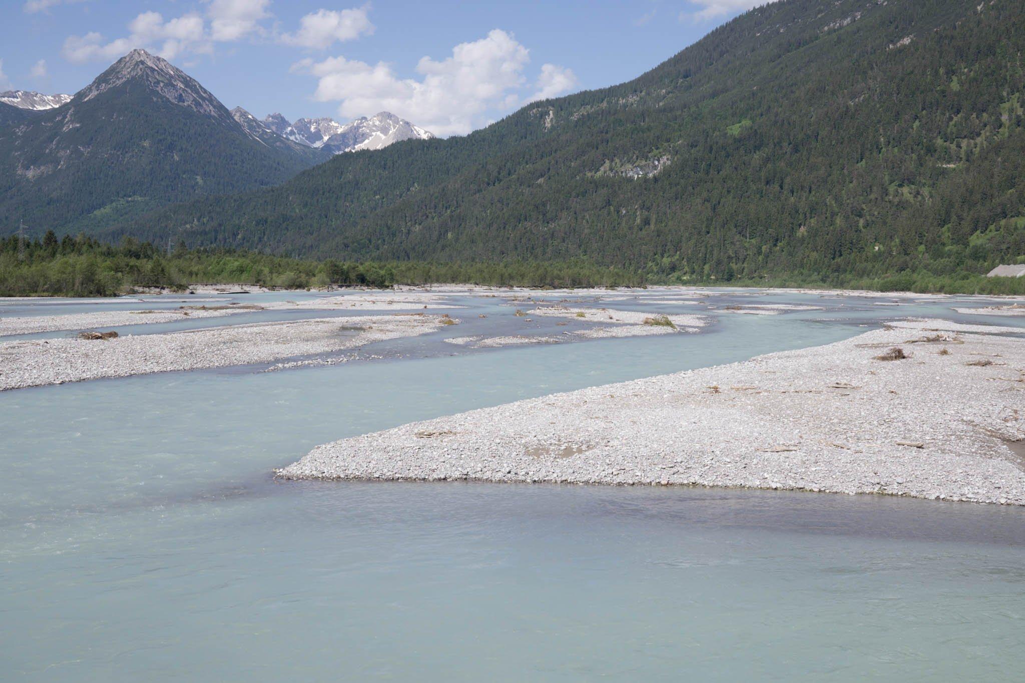 Fluss Tiroler Lech mit türkisfarbenem Wasser und Schotter mit Bergen im Hintergrund.