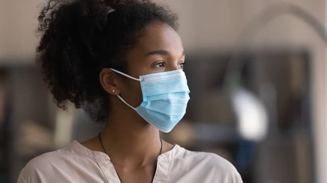 A young woman wears a so-called surgical mask and looks to the side