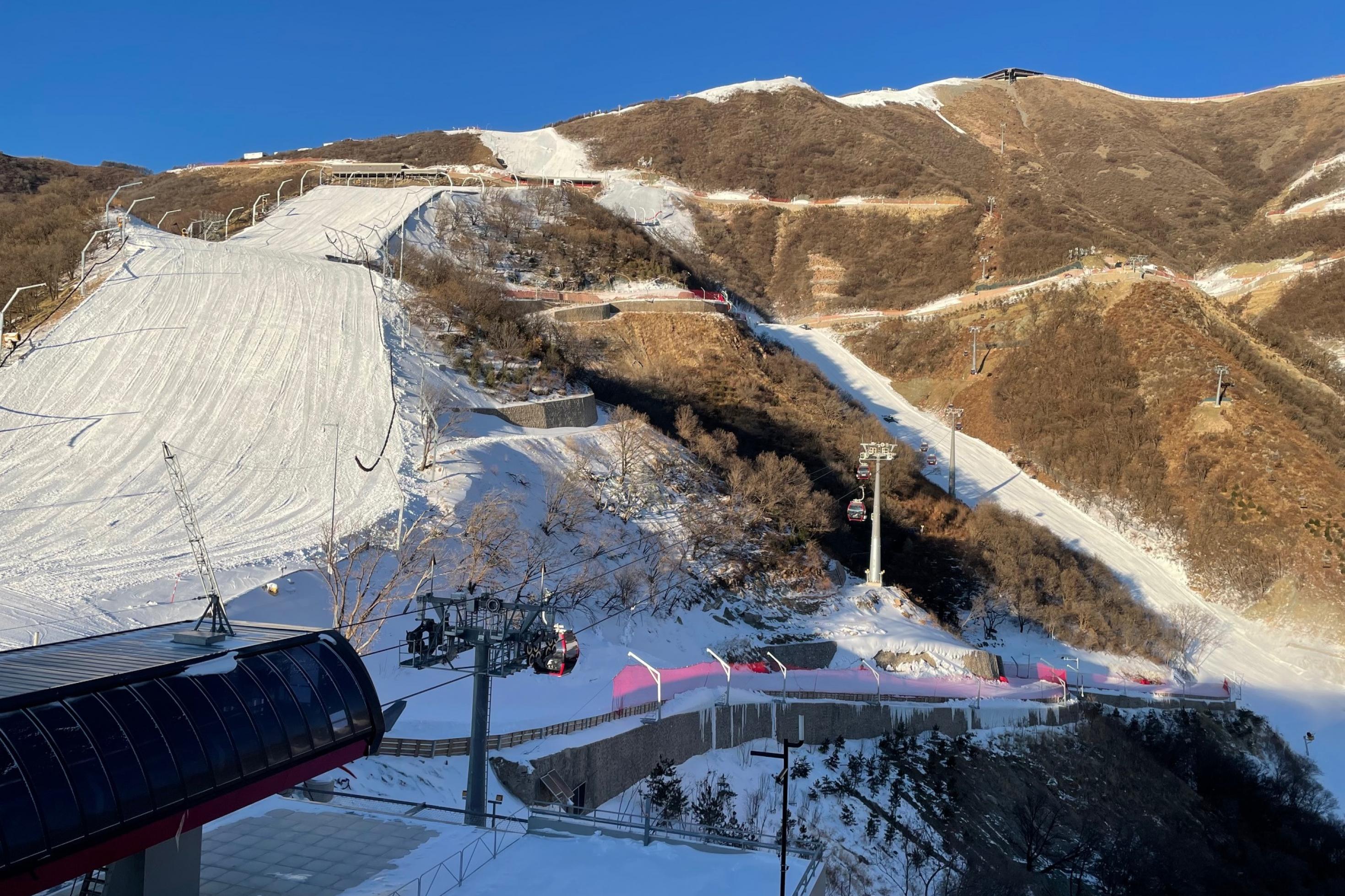 Panoramablick auf einen Skilift bei Peking. Wegen der Trockenheit müssen die Pisten für die Olympischen Winterspiele mit Schneekanonen beschneit werden. Das Terrain außerhalb der Pisten ist braun.