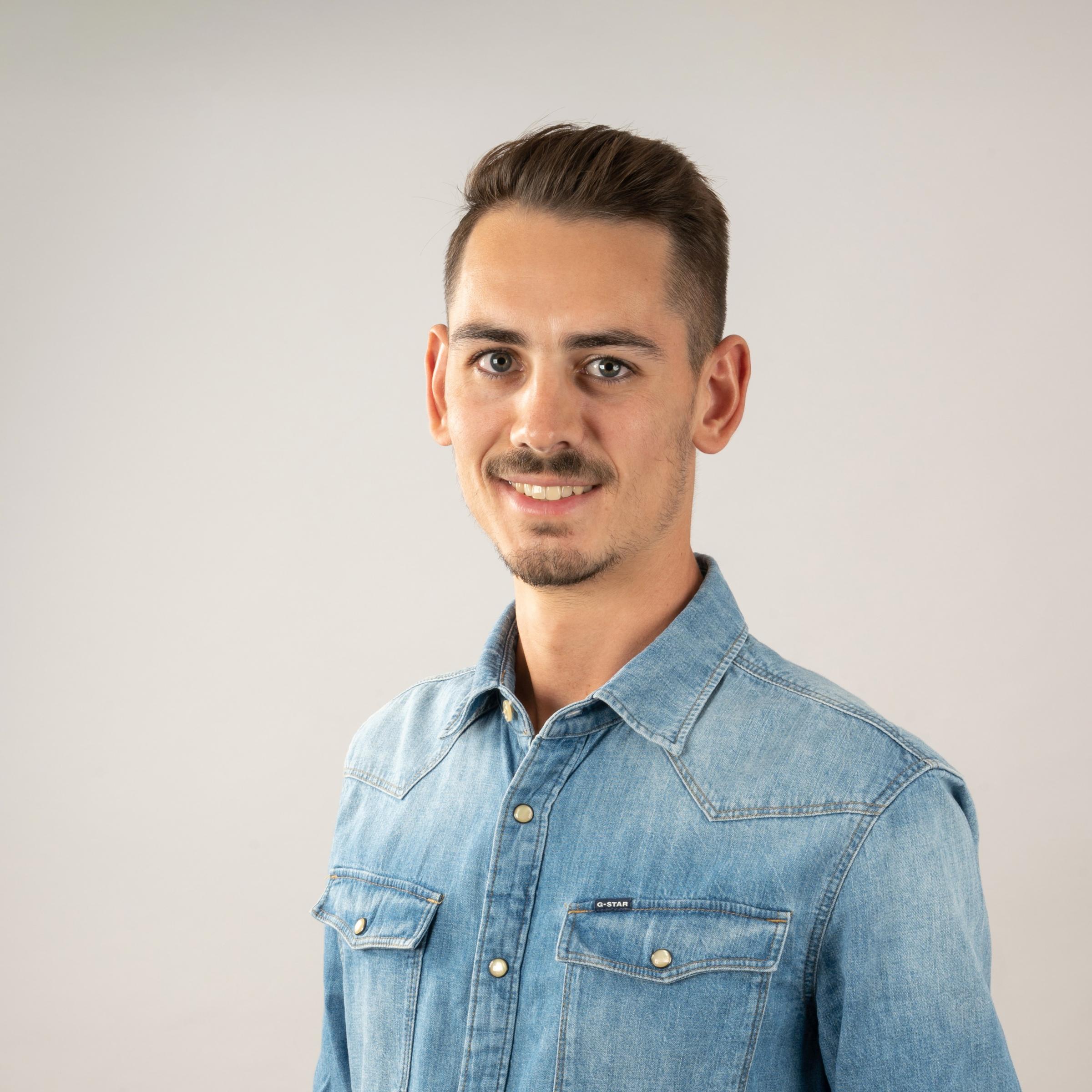 Das Bild zeigt ein Portraitbild von Nicolas Kaufmann, ein Autor der ein Jeans-Hemd trägt in frontaler Seitenansicht.