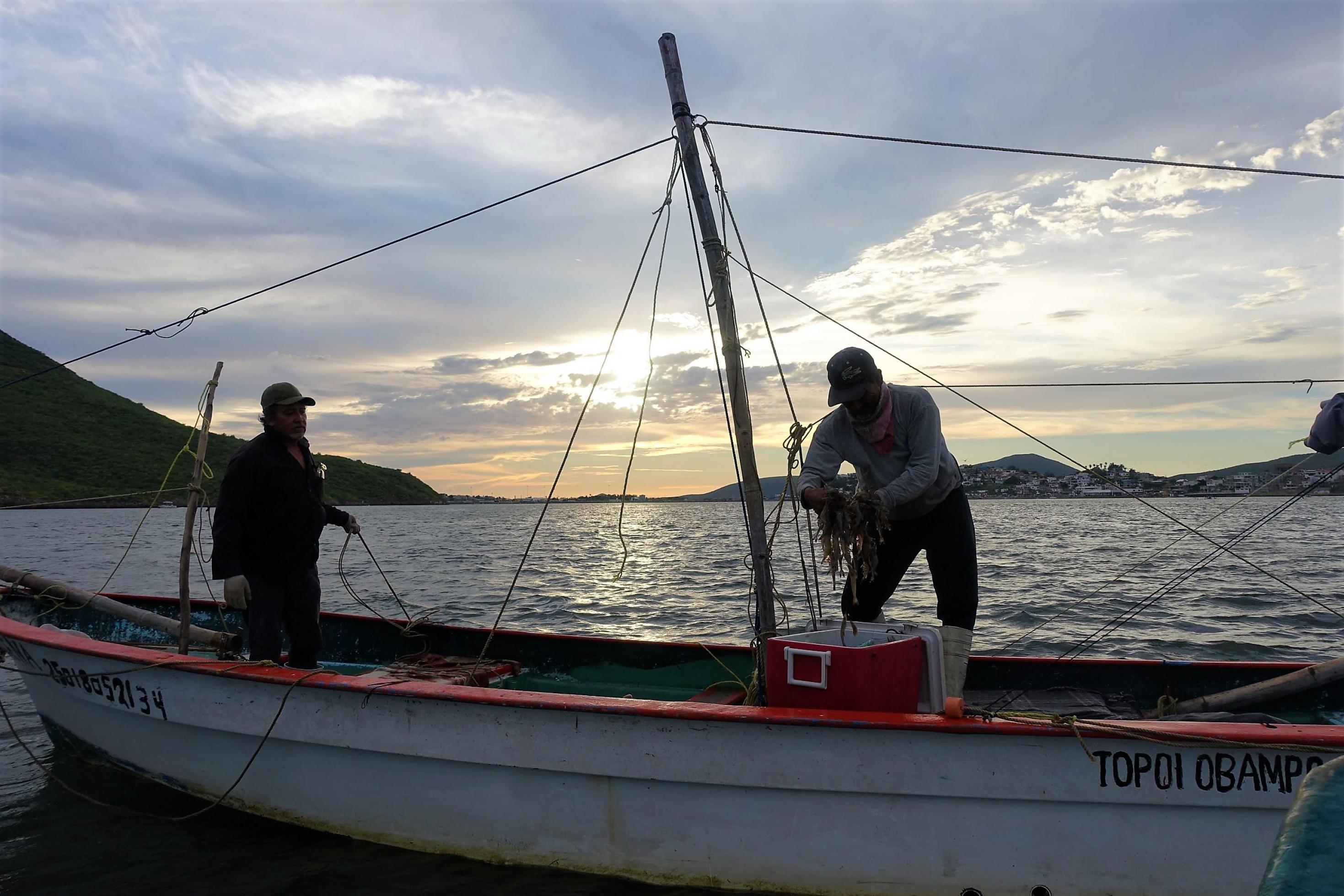 Zwei Mexikaner stehen in der Abenddämmerung auf ihrem Fischerboot in der Bucht von Ohuira