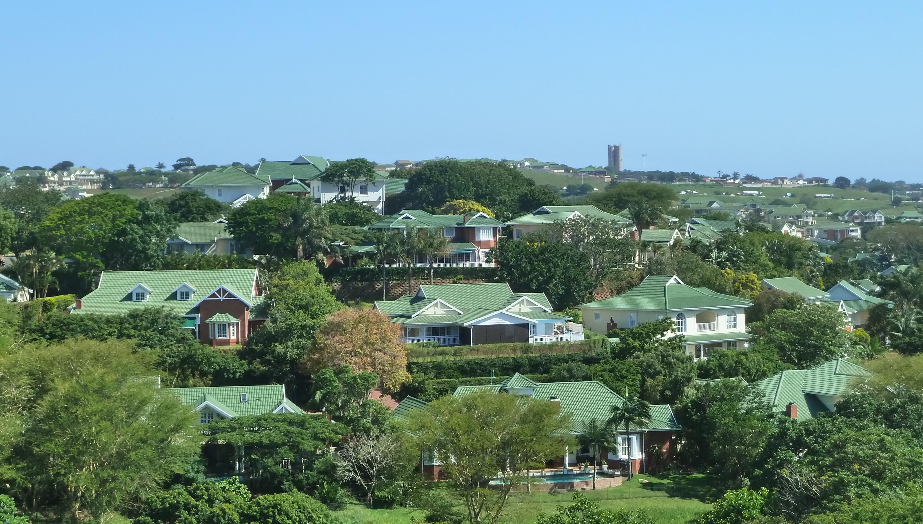 Blick auf die Häuser des Mount Edgecombe Country Club Estate 2 in Durban, Südafrika. Wohngegend mit vielen Bäumen und grünen Hausdächern .