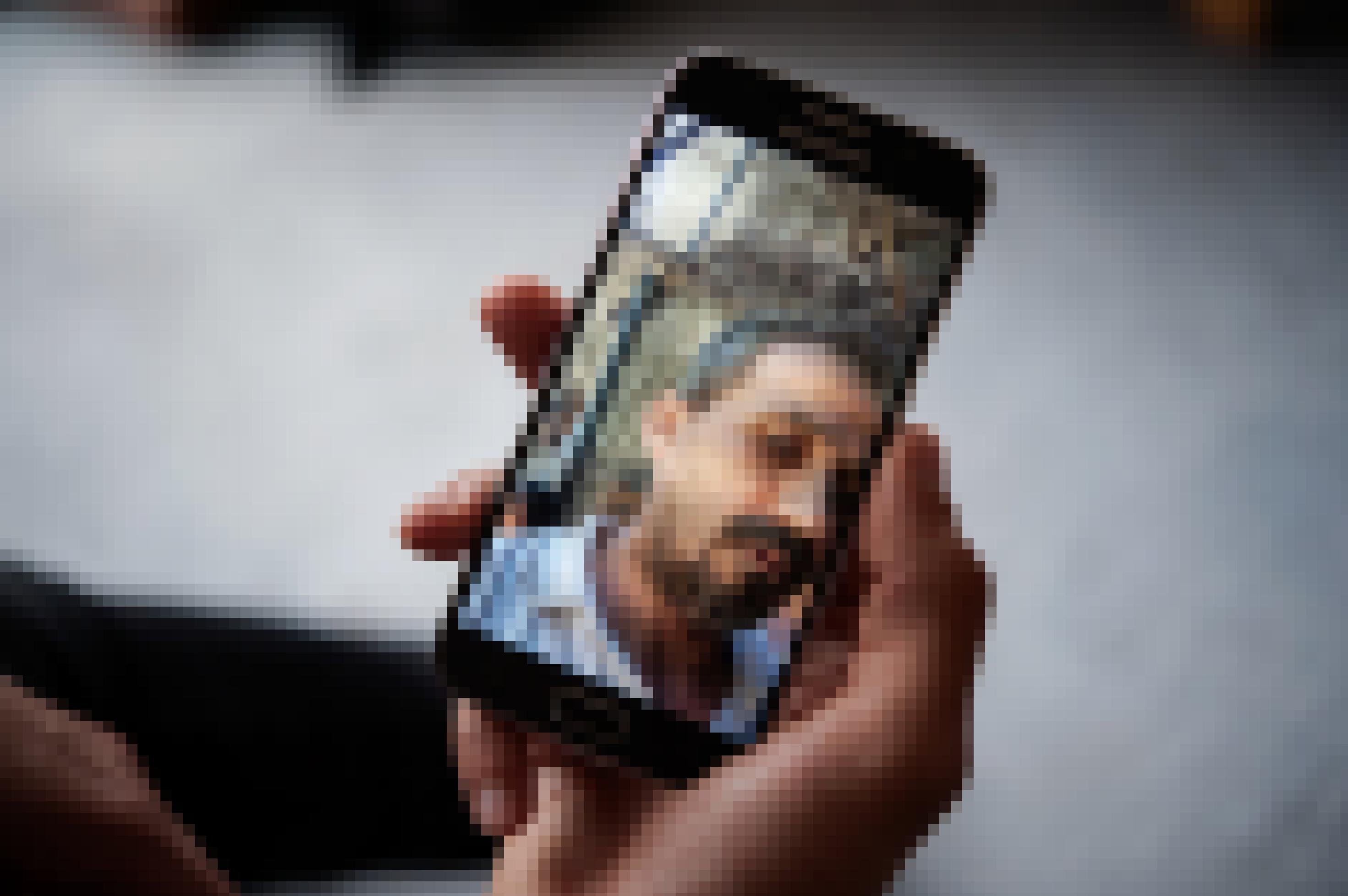 Eine Hand hält ein Smartphone, auf dem Display sieht man ein Foto, auf dem ein Mann im Schutt eines zerstörten Hauses steht.