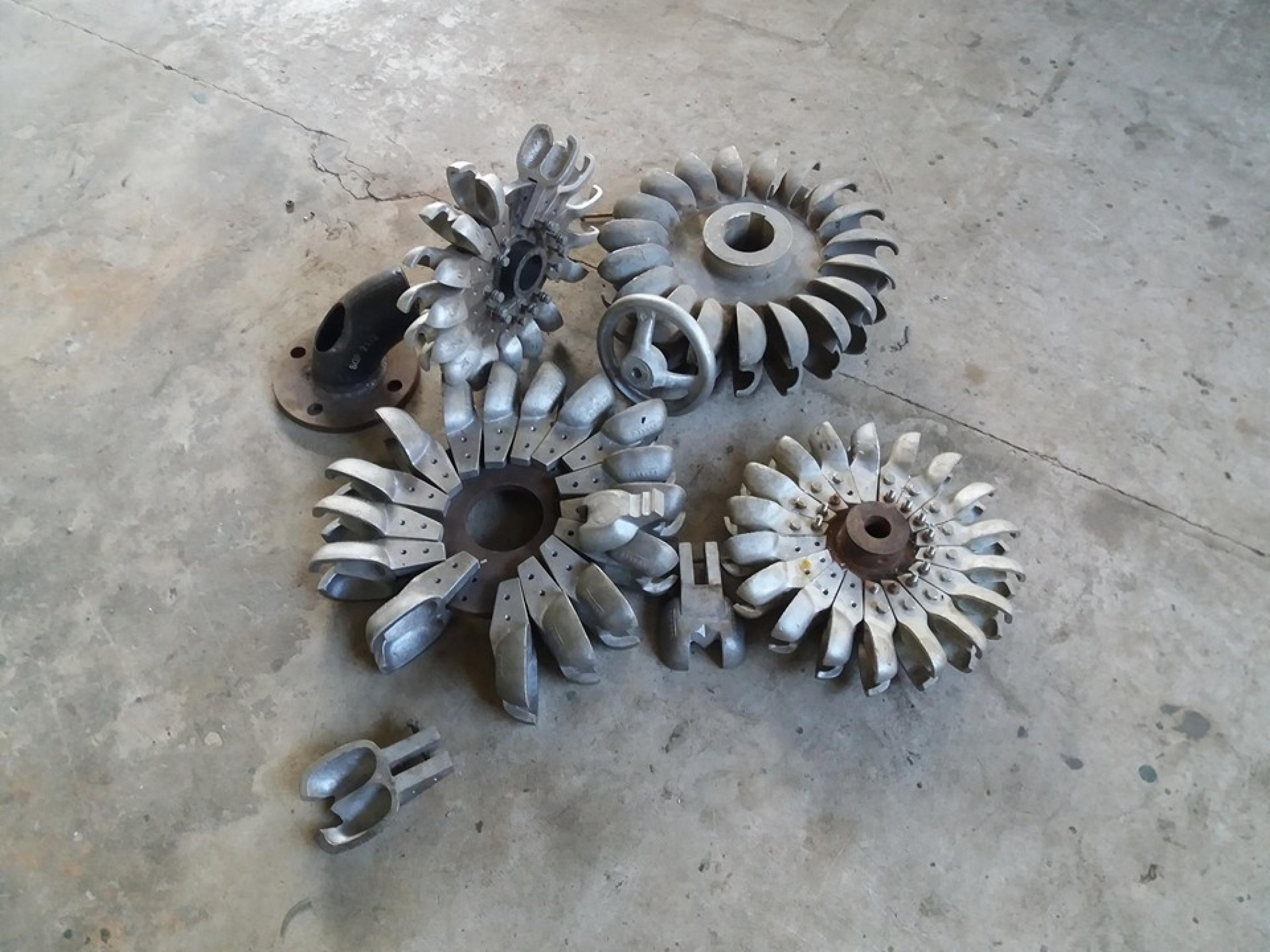 Das Bild zeigt einige Aluminium-Schaufelräder auf einen Betonboden. – Der Rotor einer Pelton-Turbine wird aus einigen Dutzend Aluminum-Schaufeln zusammengesetzt, die die Mitarbeiter bei Tonibung in Penampang/Malaysia selbst aus leeren Getränkedosen gießen. …