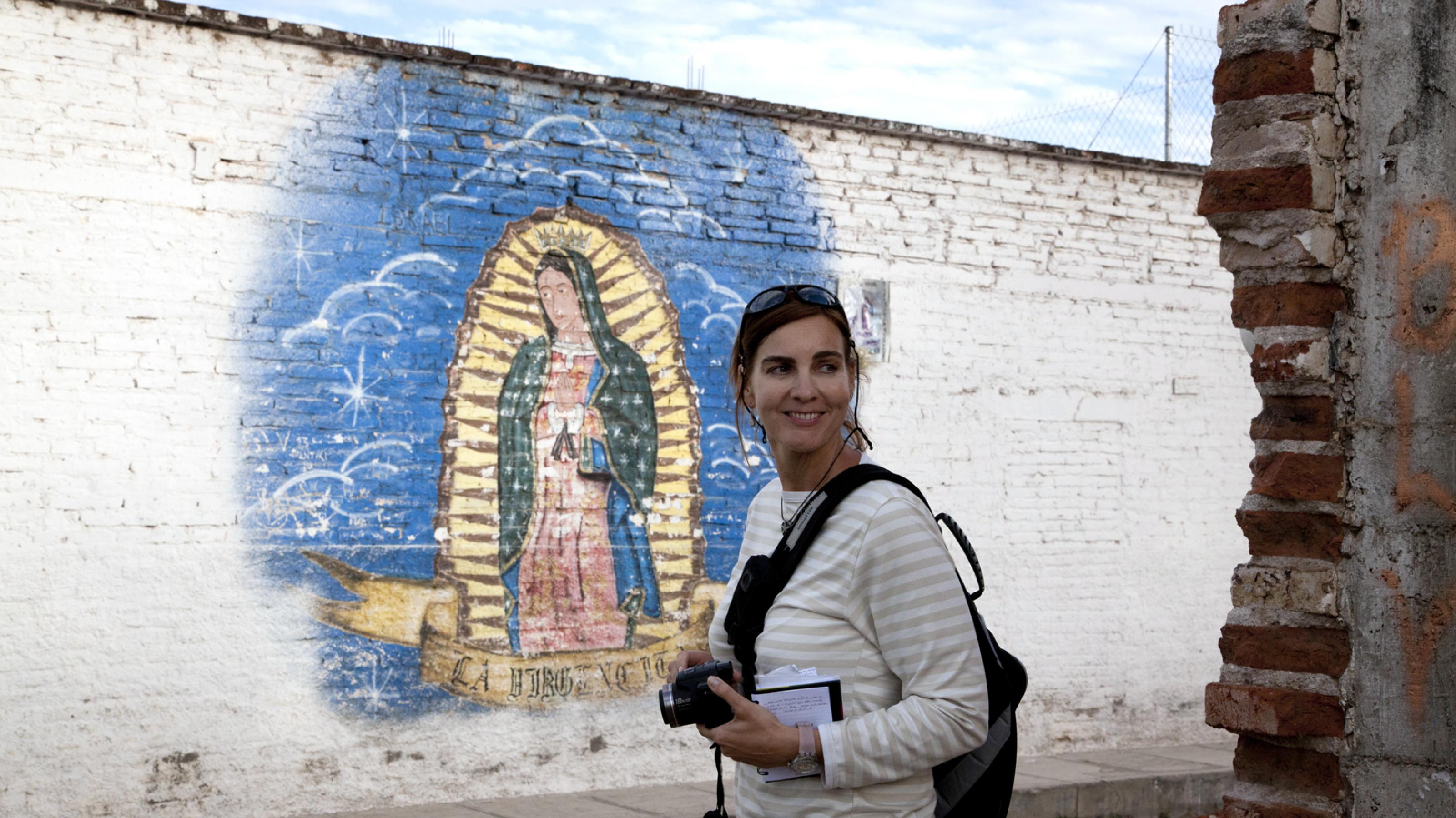 Sandra Weiss mit Fotoausrüstung vor einer mit Graffiti bemalten Wand in Mexiko.