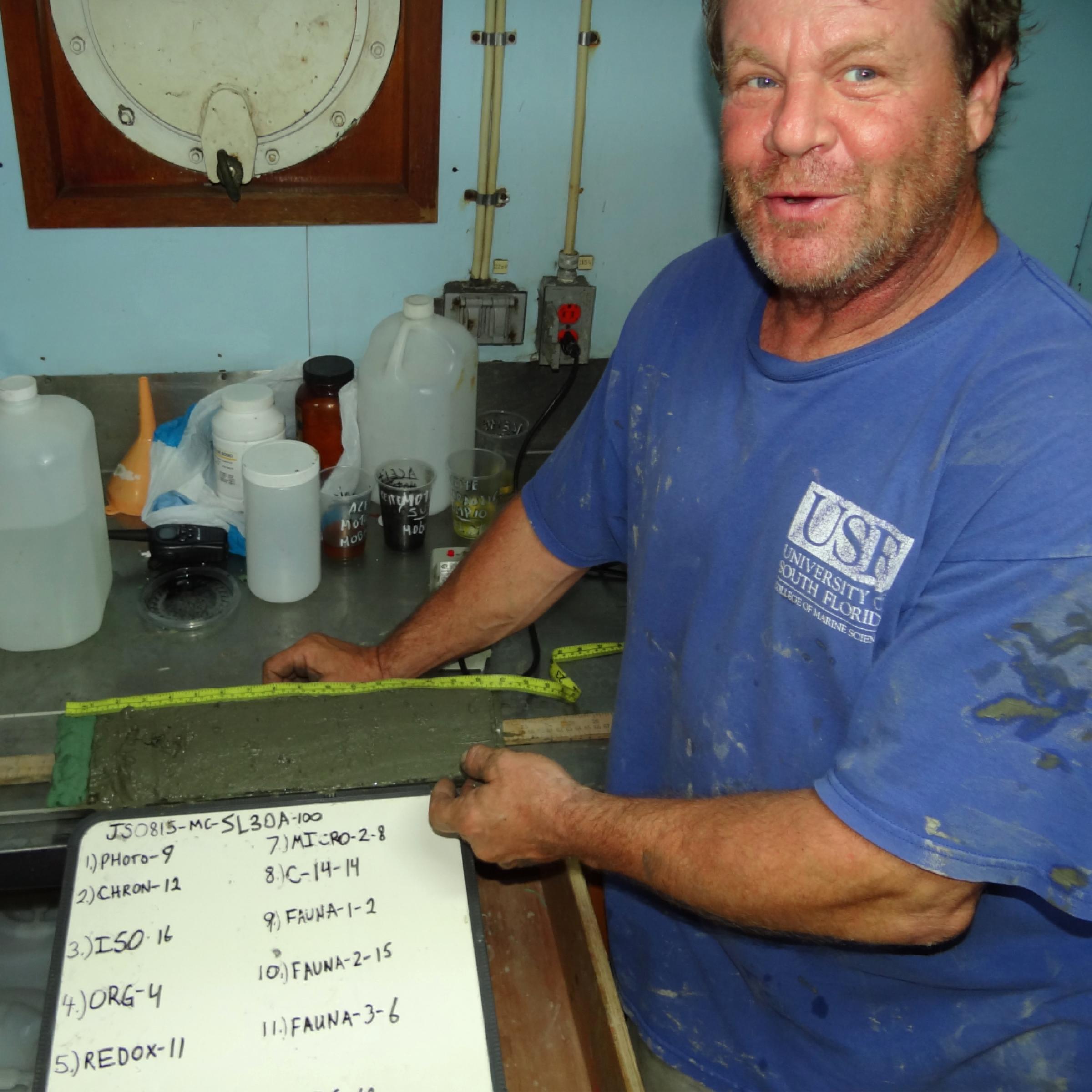 David Hollander steht im Schiffslabor vor einem Schnitt durch einen Sediment-Bohrkern.