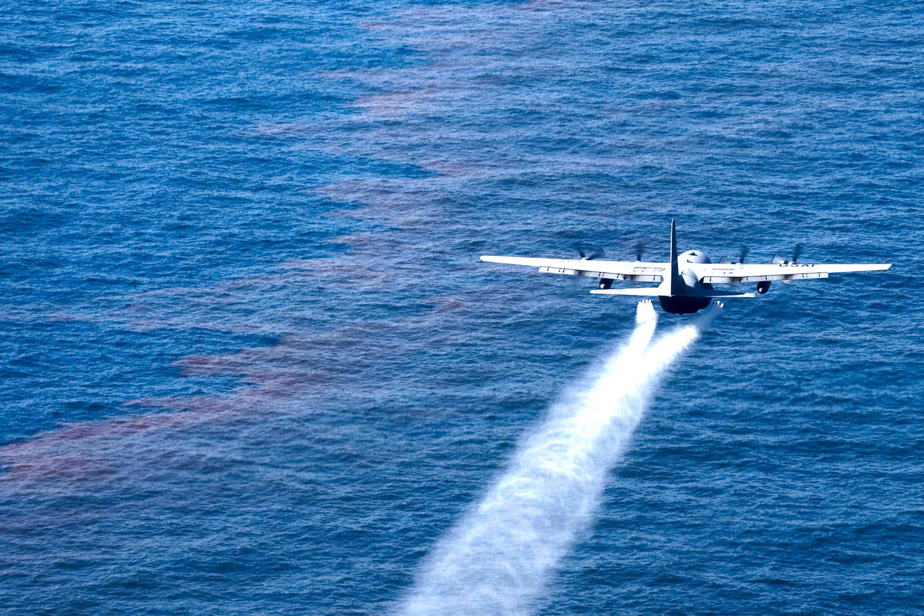 Flugzeug versprüht Flüssigkeit über Ölteppich auf dem Meer.